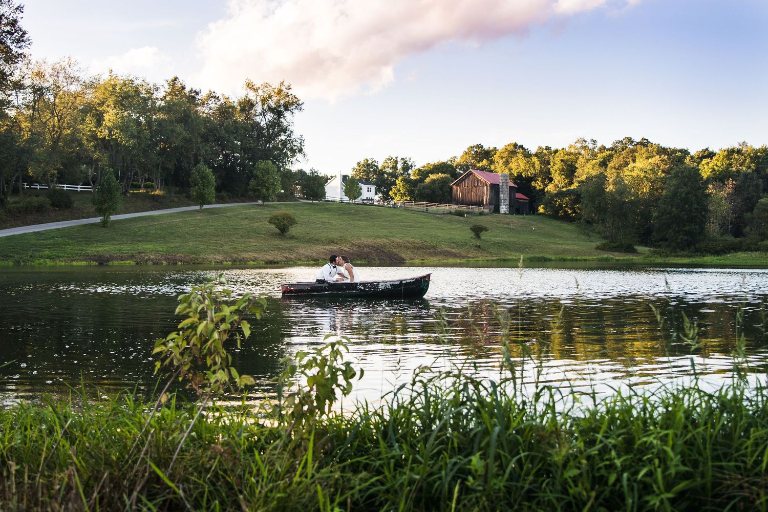 A small boat floats on a serene lake surrounded by green grass and trees during a peaceful summer evening.