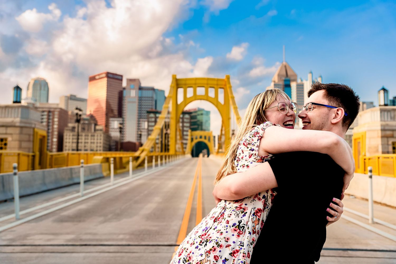 A couple embraces on Pittsburgh's iconic yellow Roberto Clemente Bridge with the downtown skyline in the background.