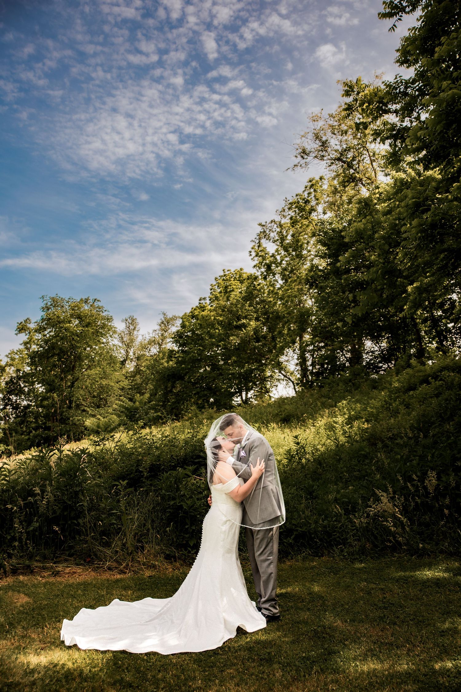 A couple shares romantic moments under a cloudy sky in a natural setting with trees during their wedding photo session.
