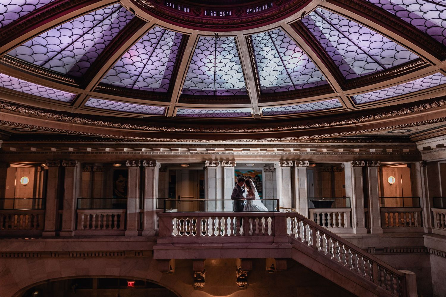 Elegant domed rotunda with stained glass ceiling and ornate wooden balustrades inside a historic building interior.