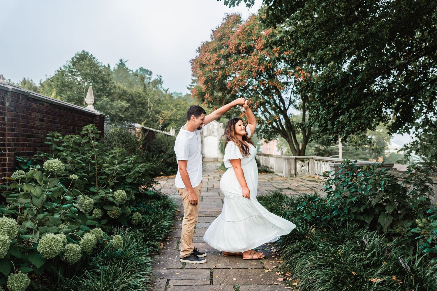 A couple dancing together on a garden path surrounded by lush greenery and blooming hydrangea bushes.