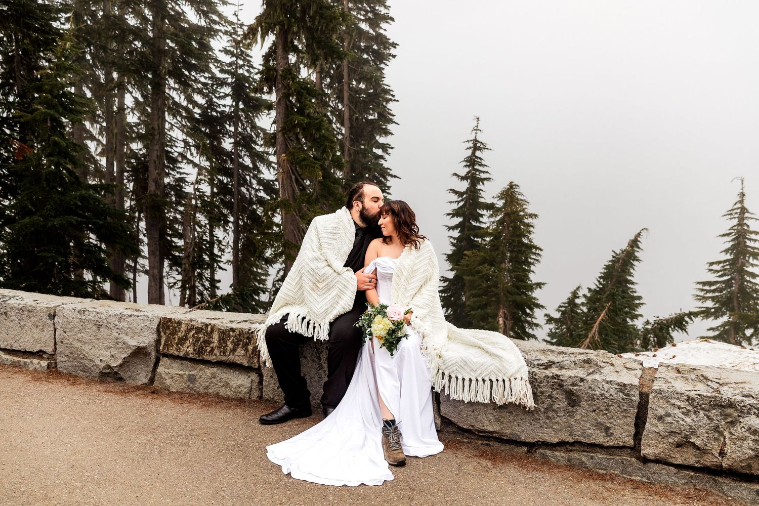A couple shares romantic moments in a mountain setting against a snowy landscape and evergreen trees in the background.