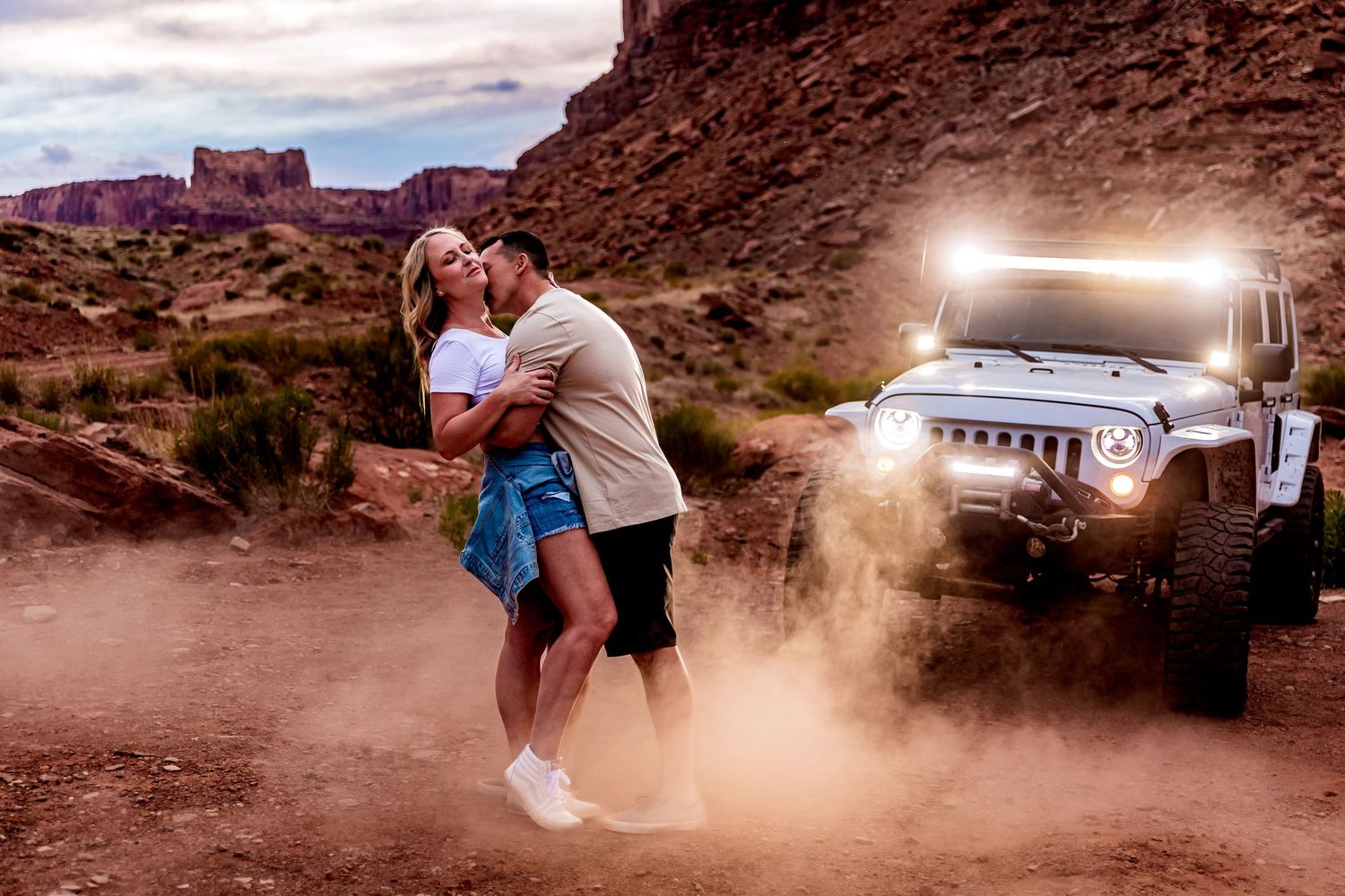 Car kicks up dust cloud while off-roading on desert trail through scenic red rock canyon at sunset.