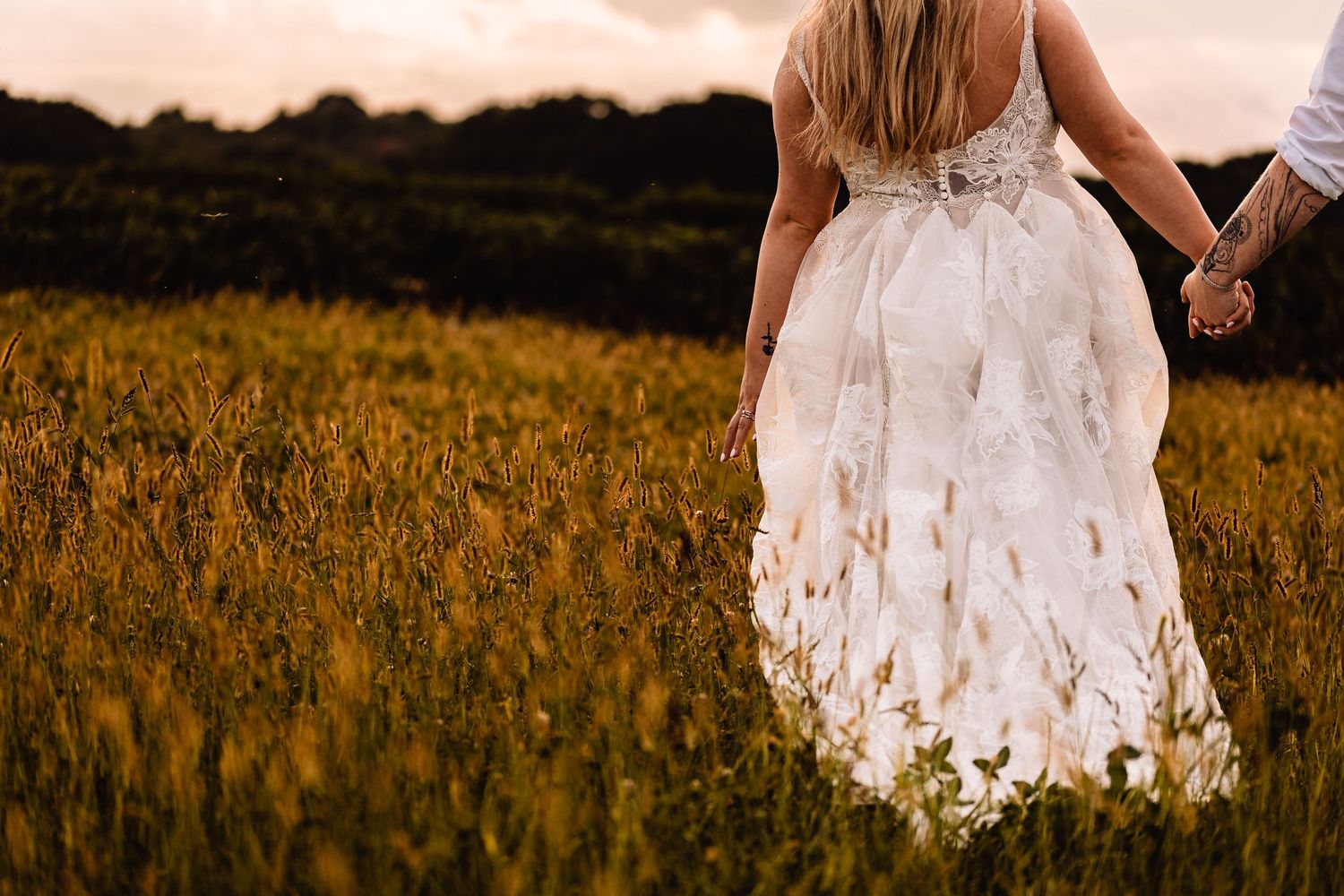 A person in a flowing white lace dress walks through a golden field at sunset.