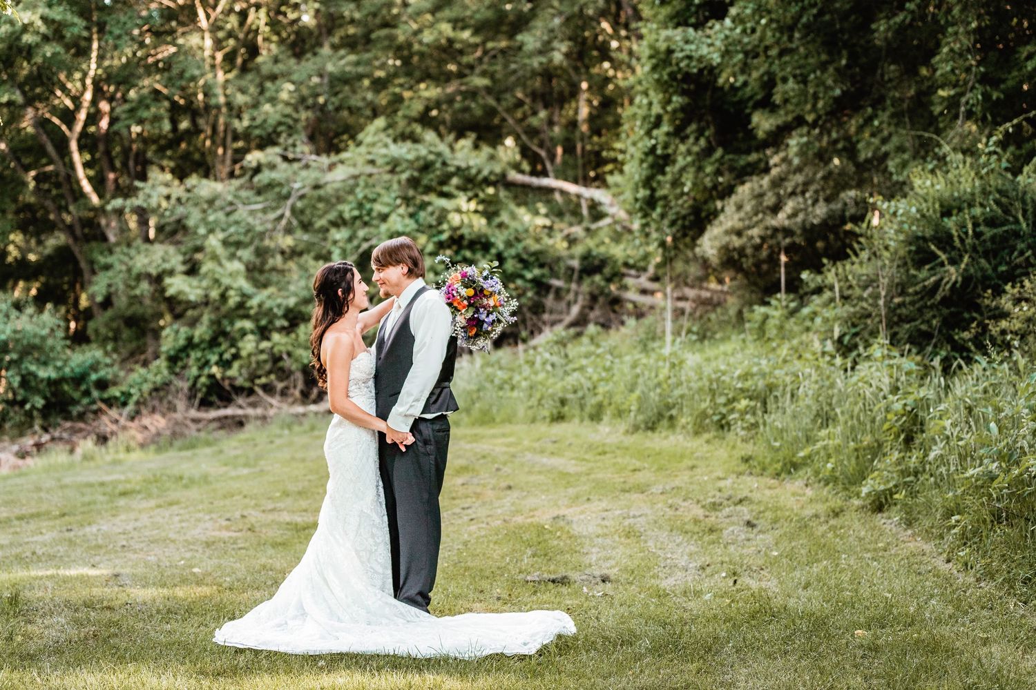 A couple embraces in a romantic outdoor wedding portrait surrounded by lush greenery and forest scenery.