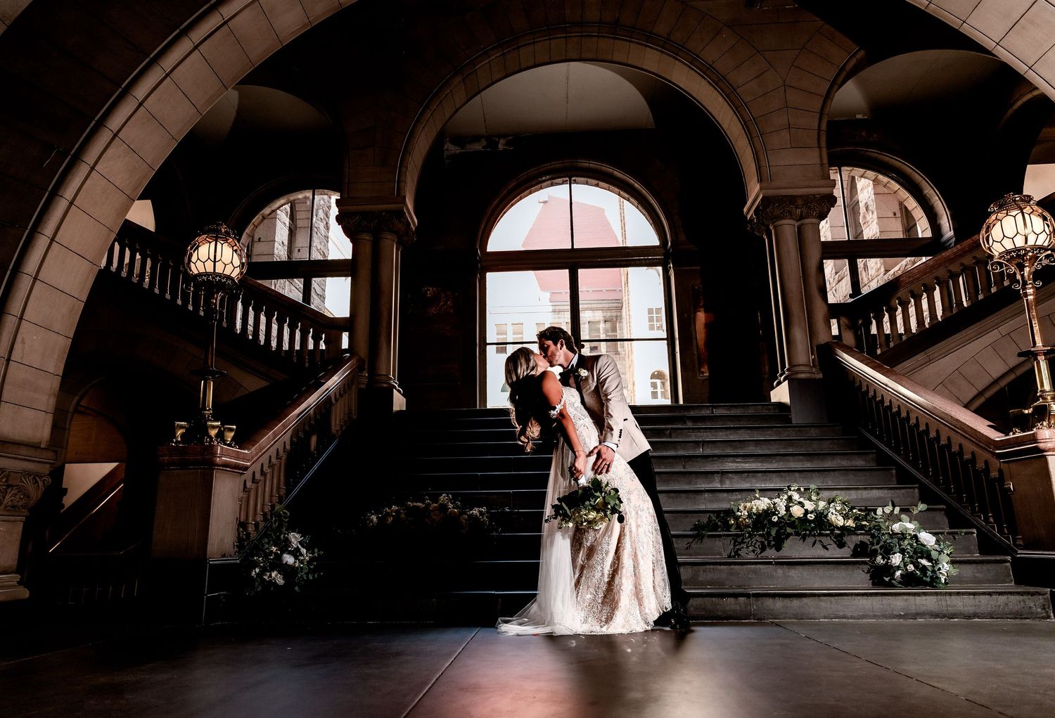 Elegant wedding kiss on grand staircase with floral decor at historic venue | luxury wedding photo inspiration
