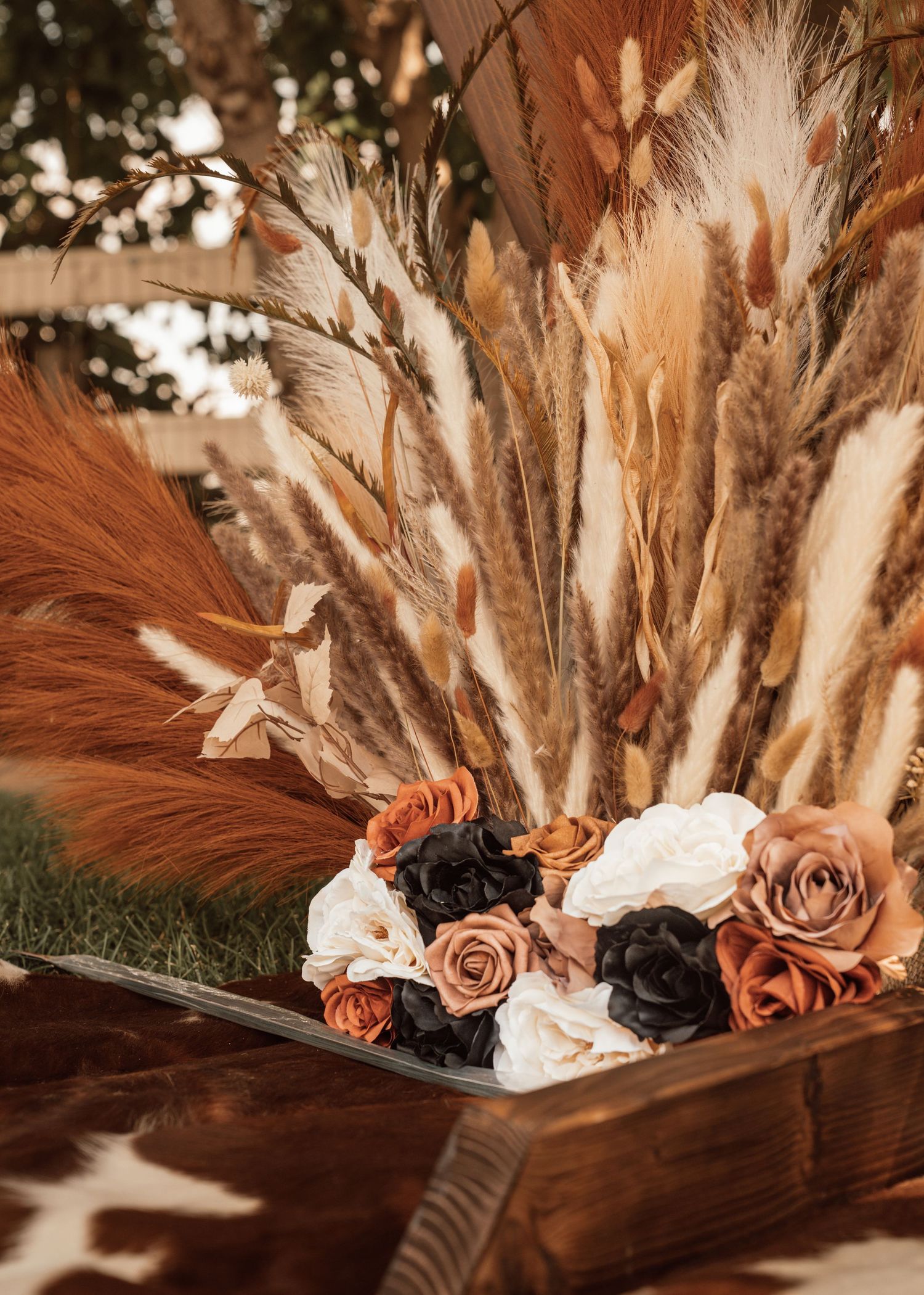 Rustic wooden box arrangement with dried pampas grass, roses in autumn tones, and boho floral elements.