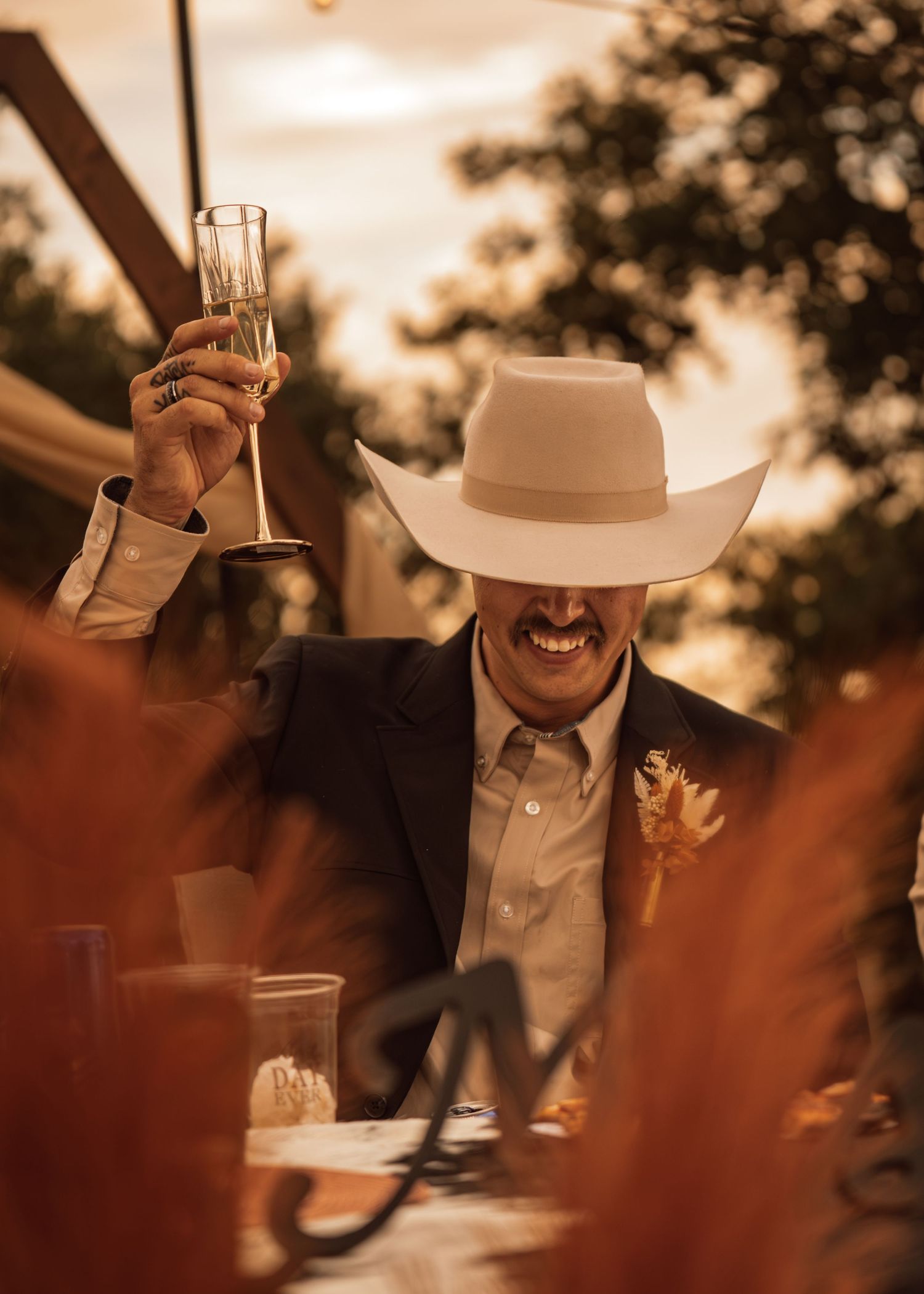 A person in a cowboy hat raises a glass during a sunset celebration outdoors.