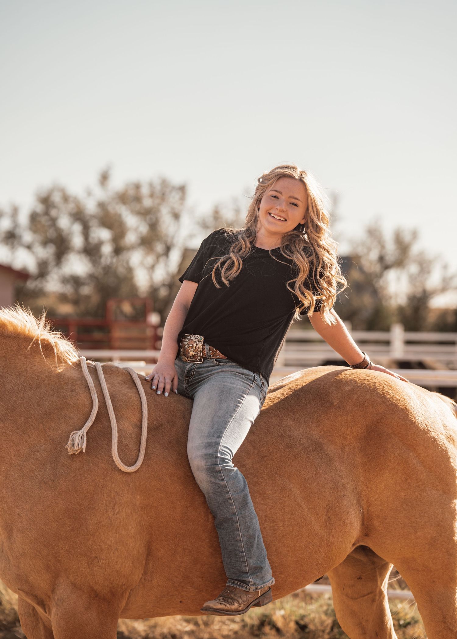 Person playfully posing on brown horse in outdoor setting with natural lighting.