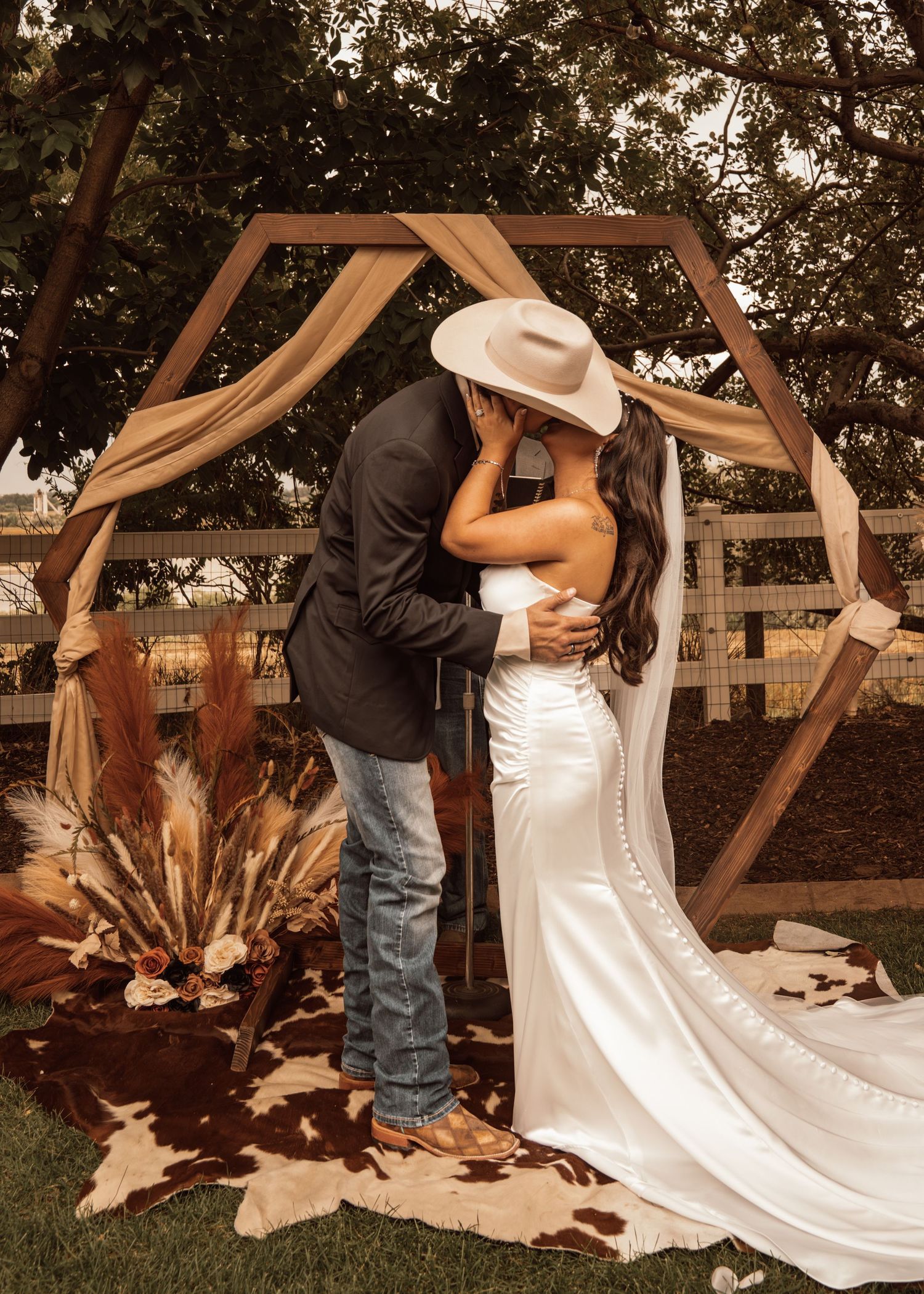 A romantic couple shares a dip dance pose in front of a wooden geometric backdrop at an outdoor wedding venue.