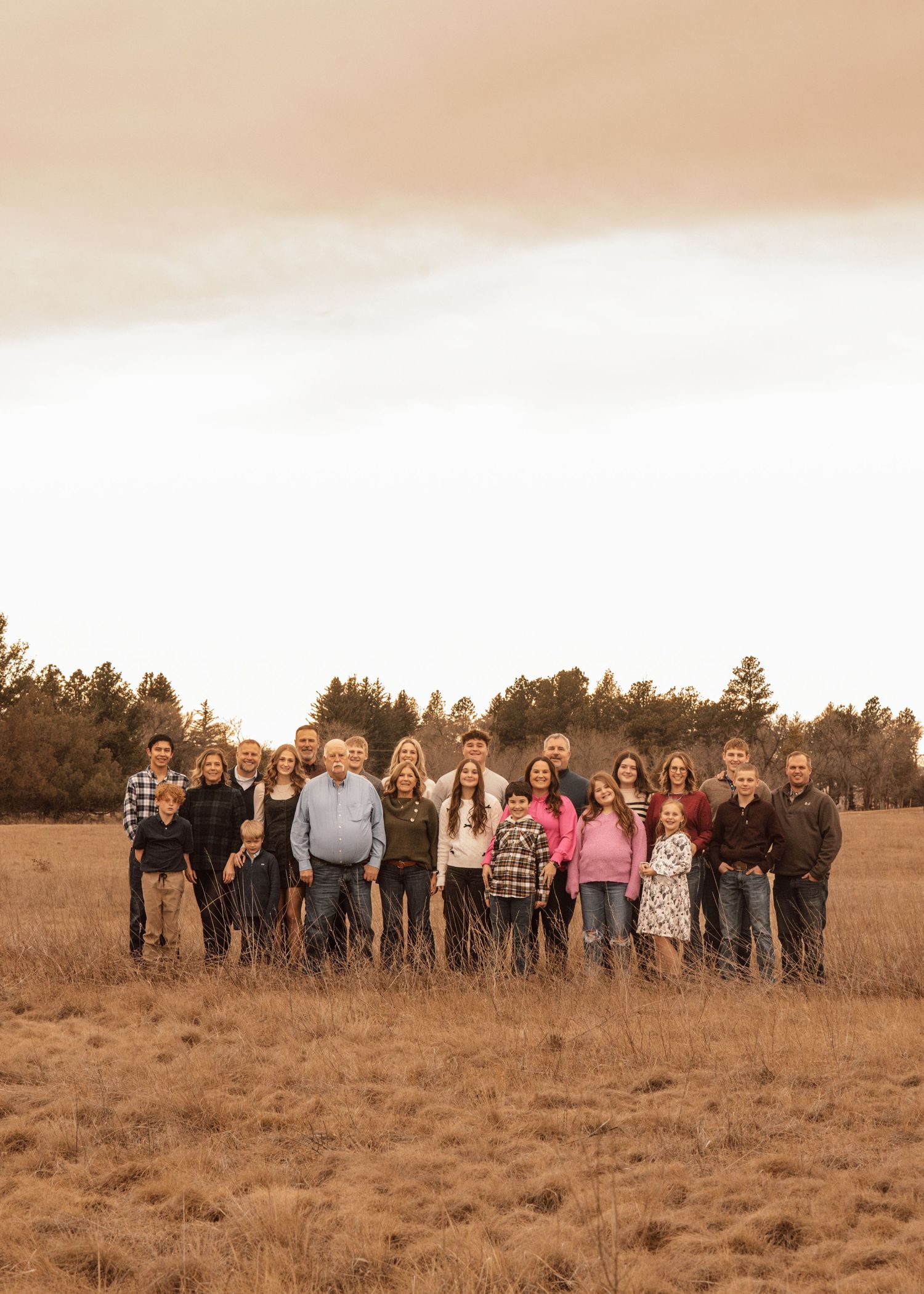 Group photo of people lined up in an open field with evergreen trees silhouetted against the sky.