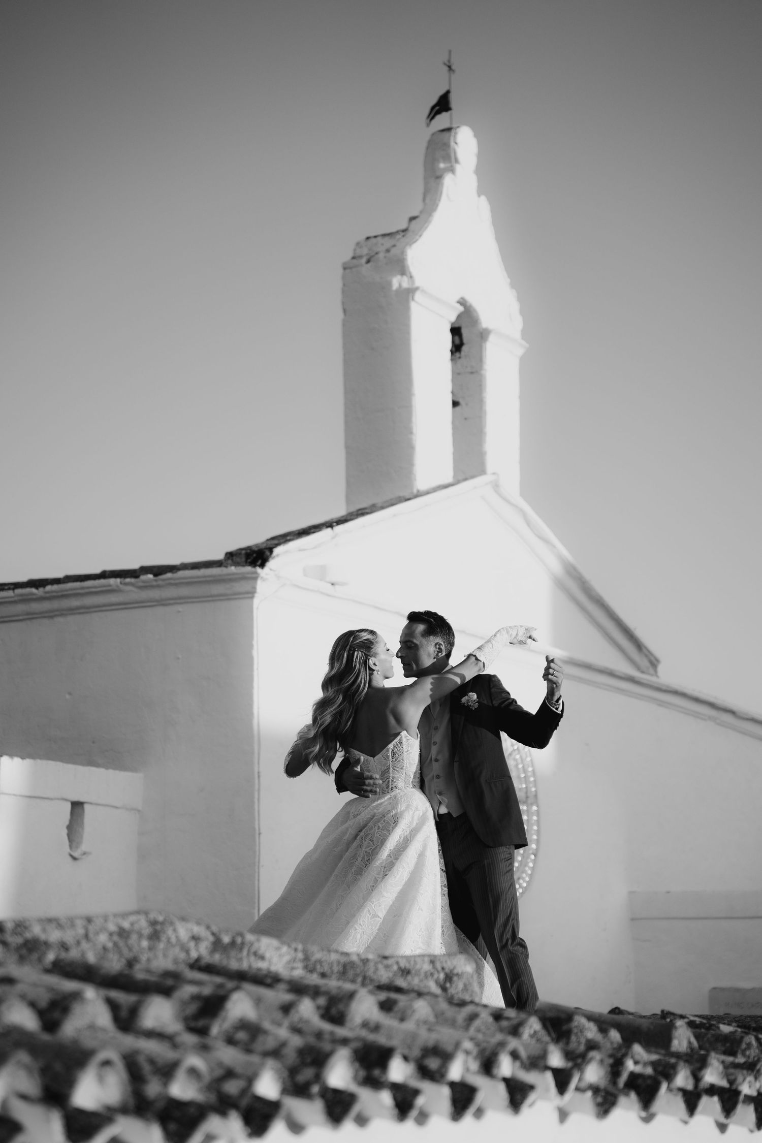 A couple dances and poses in front of a white Mediterranean church in puglia steeple in a black and white photo series.