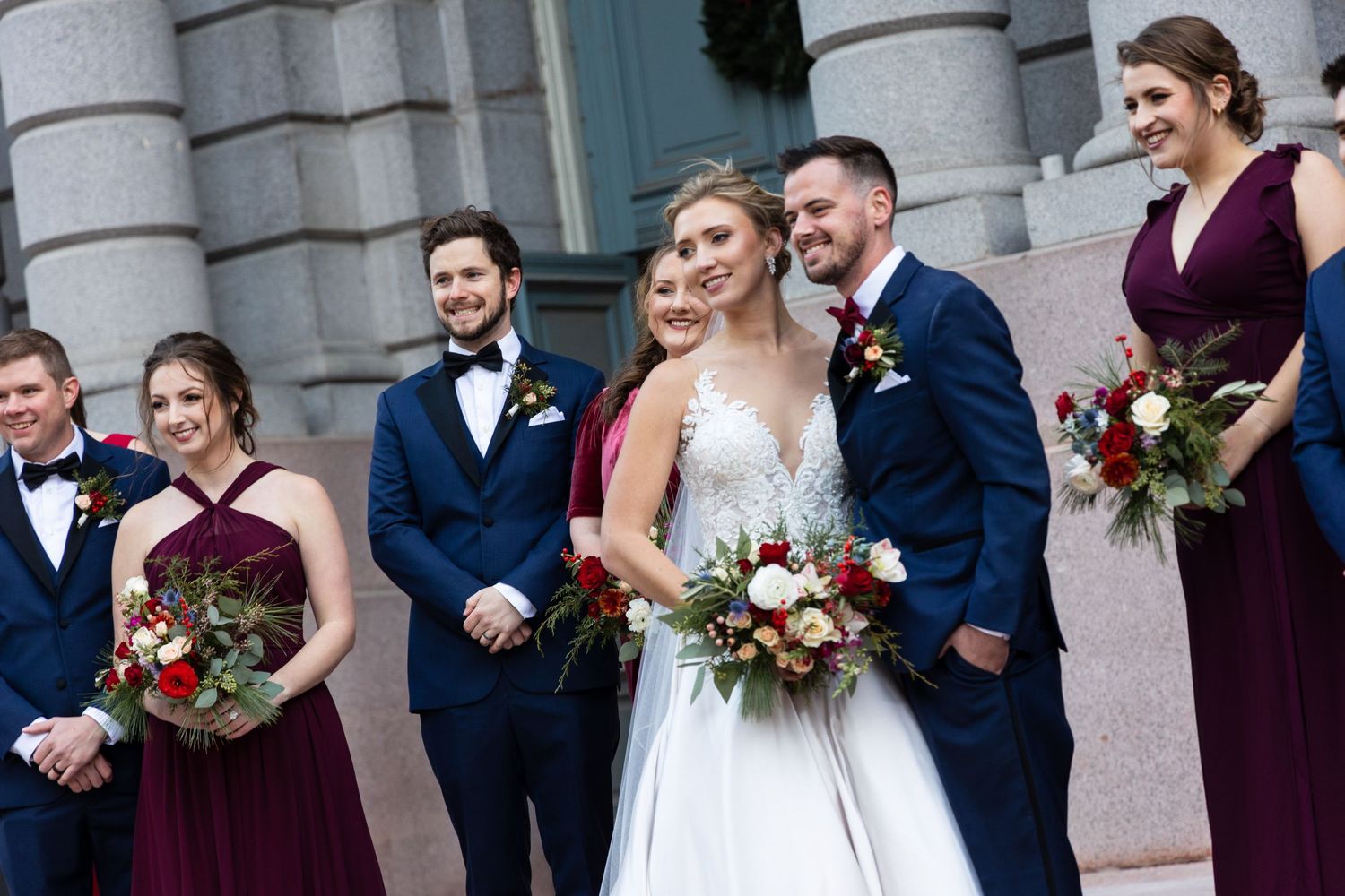 Wedding party gathers on grand stone steps with burgundy and navy color scheme.