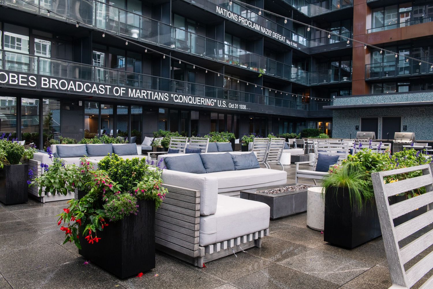 Outdoor terrace with grey lounge furniture and planters surrounded by modern architecture.