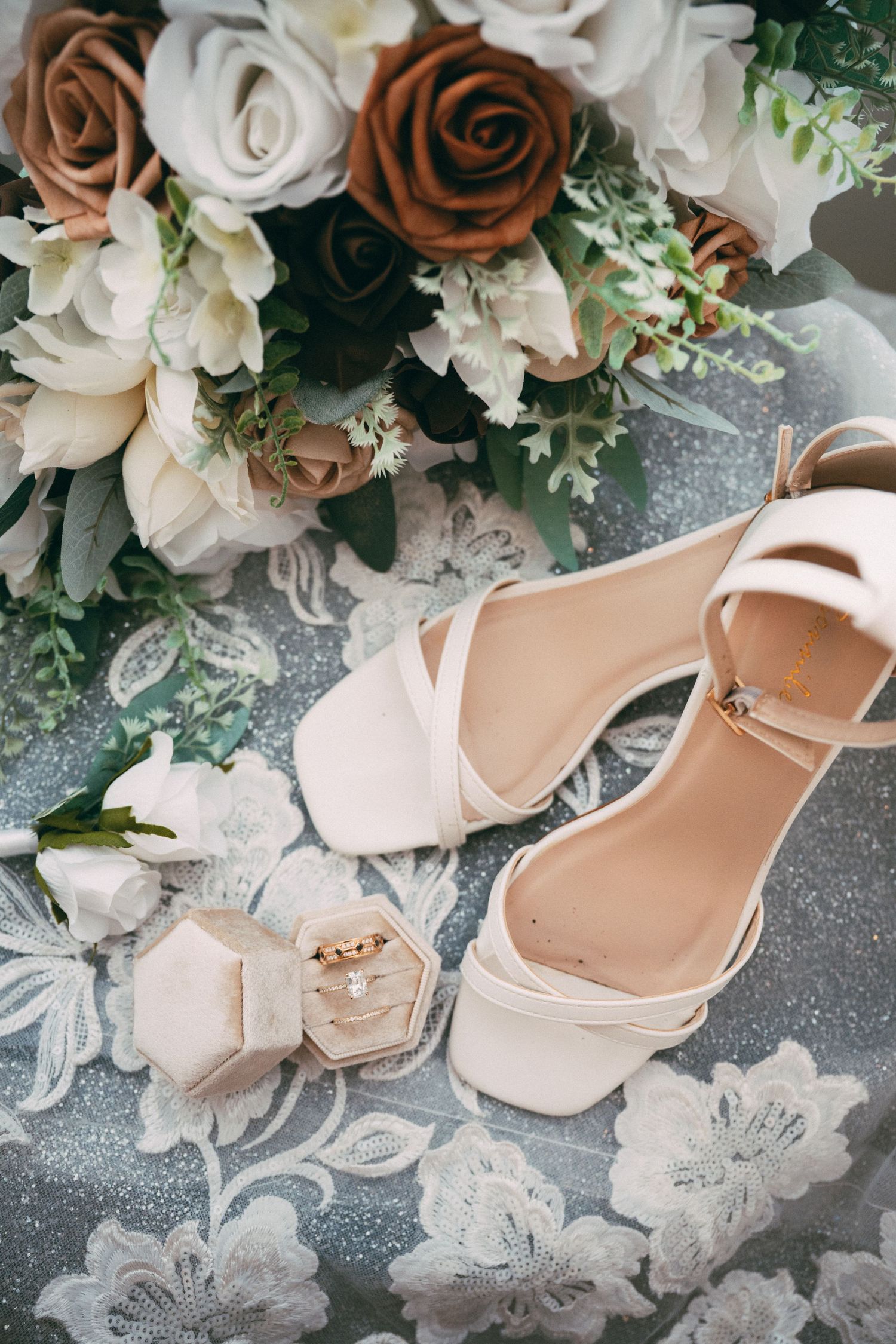 Elegant cream-colored bridal heels displayed with white and brown floral bouquets against a lace background.