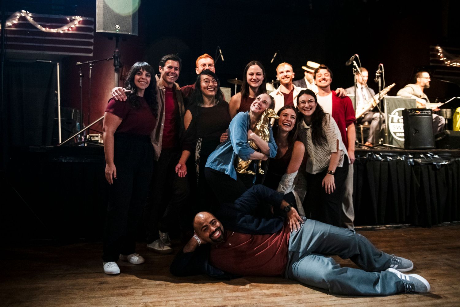 Performers strike playful poses for a group photo on stage after their show.