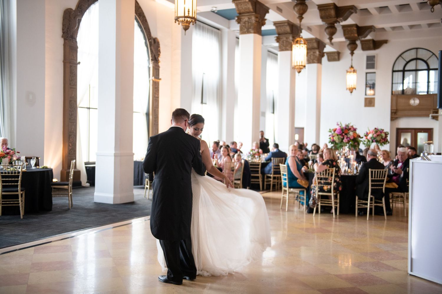Elegant ballroom wedding reception with couple dancing surrounded by dining tables and guests.