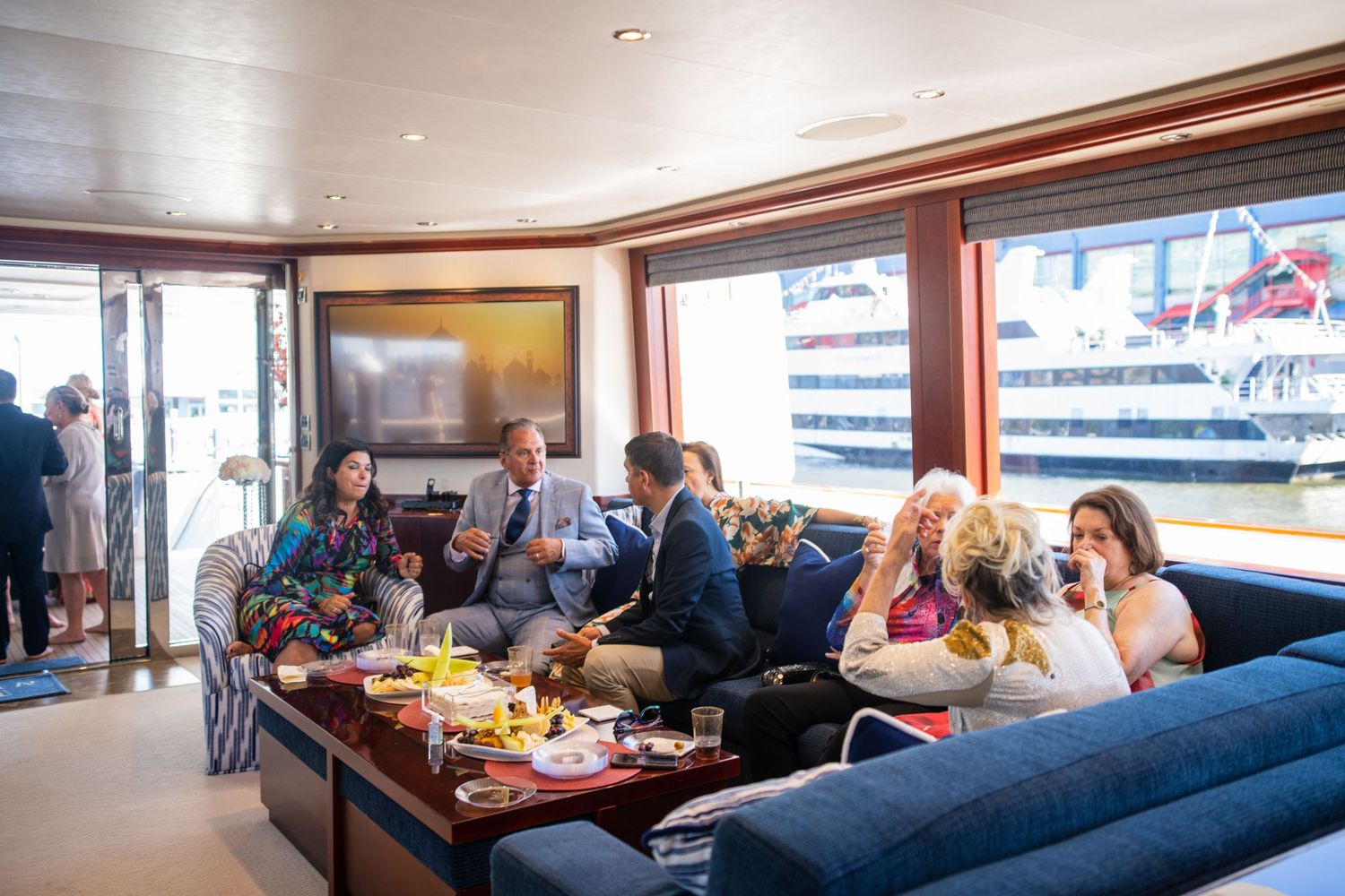 Group of guests enjoying food and drinks on a blue sectional couch aboard a yacht.