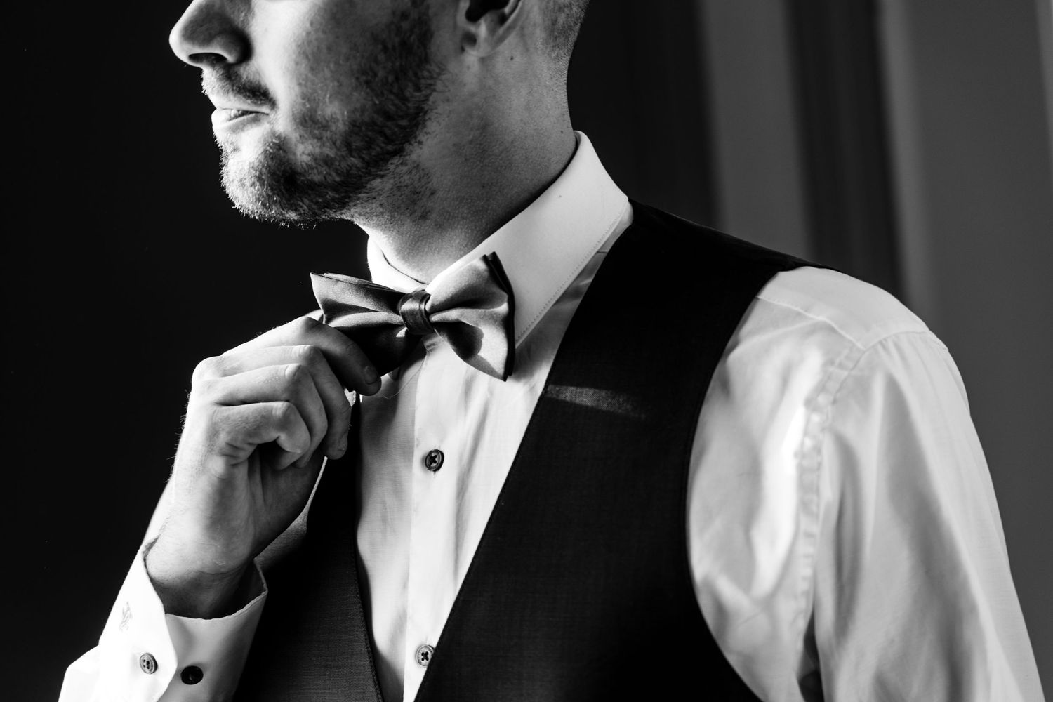 Black and white portrait of a groom adjusting his bow tie.