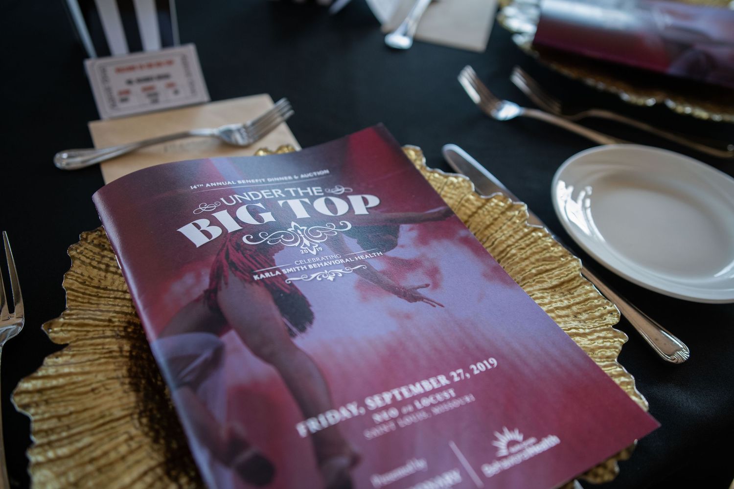 Close-up of Big Top themed event program on a gold charger plate with elegant place setting.