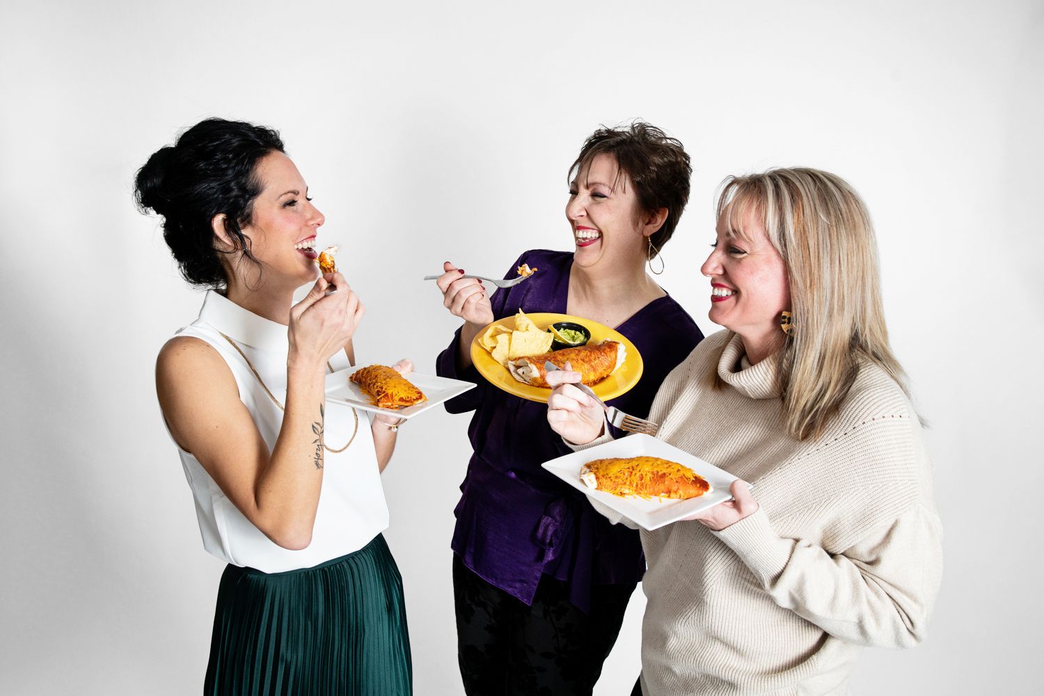 Three people in winter attire relaxing and laughing on white furniture.