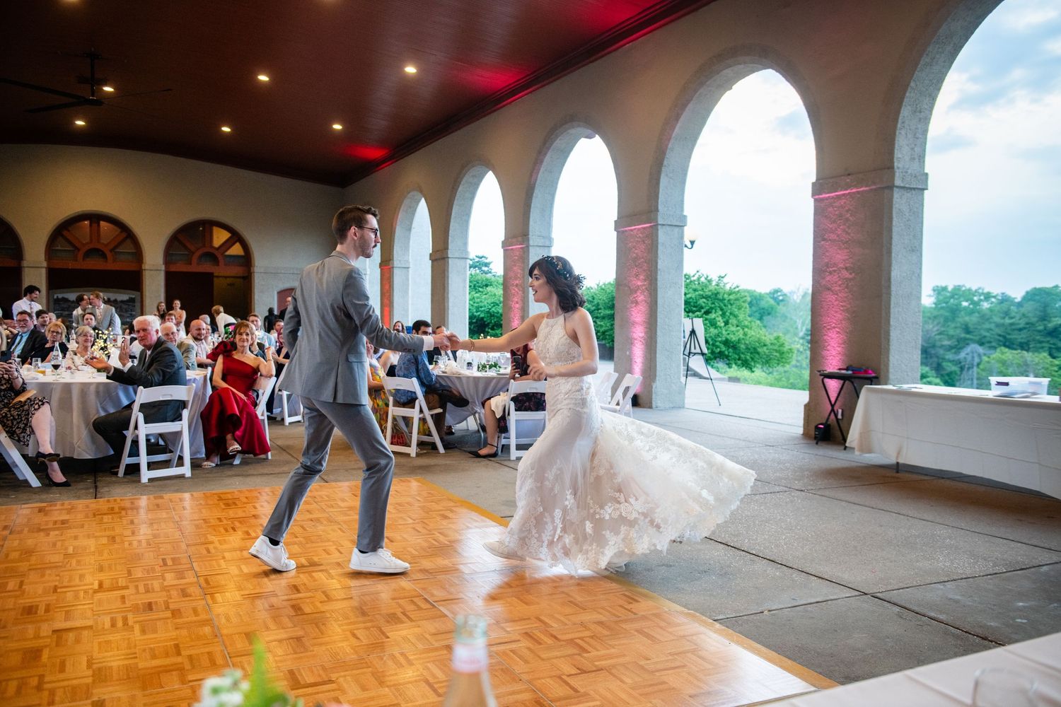 Dancing couple twirling on wooden floor during wedding reception in elegant venue with arched windows.