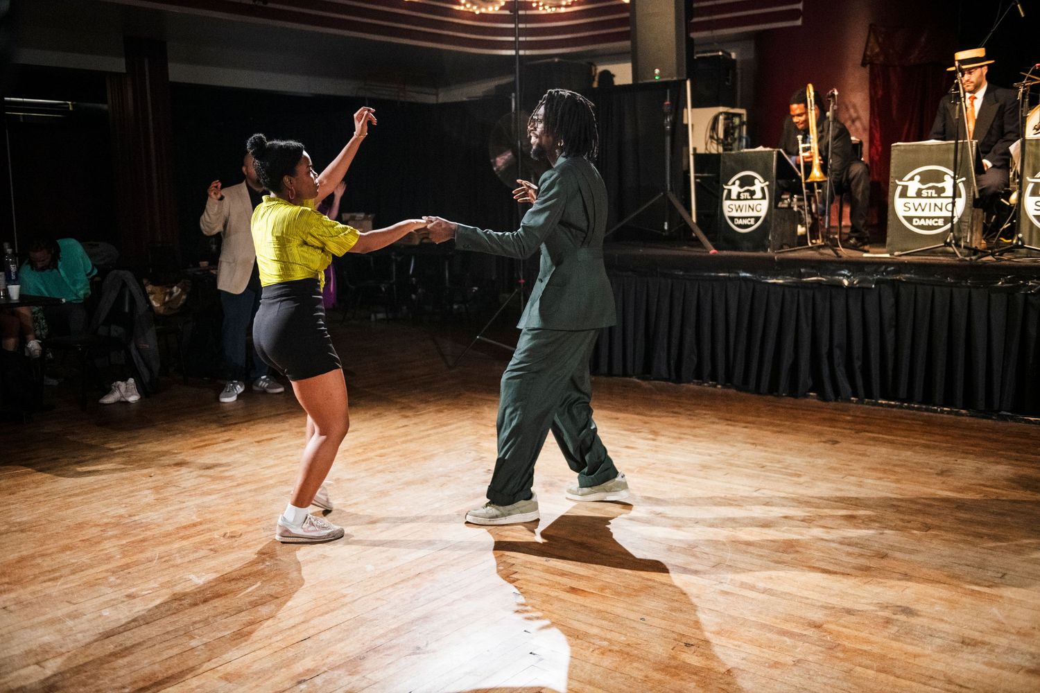Two dancers perform energetic swing dance moves on a wooden dance floor in a vintage-style venue.