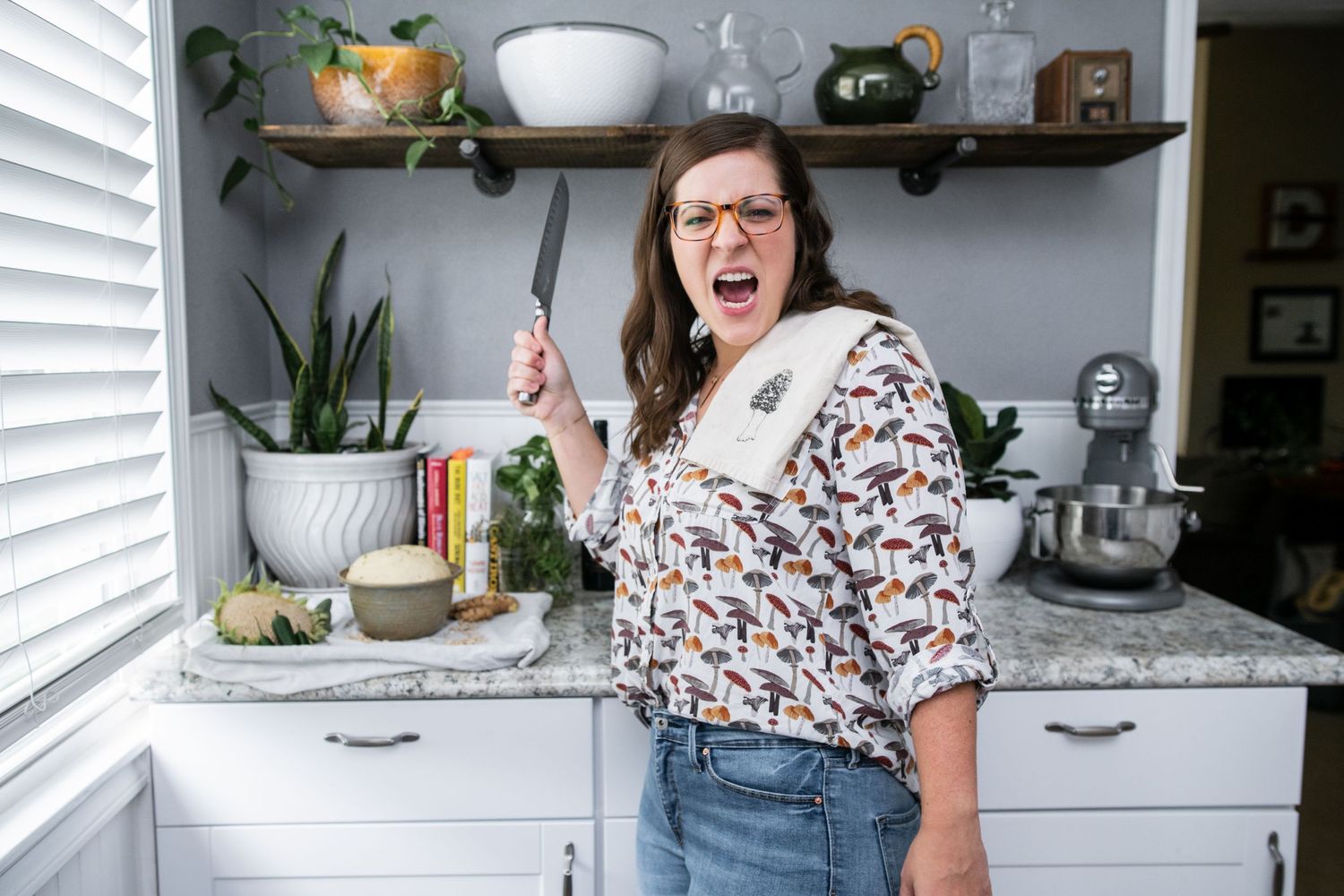 A person showing excitement while holding a knife in a kitchen with open shelving.