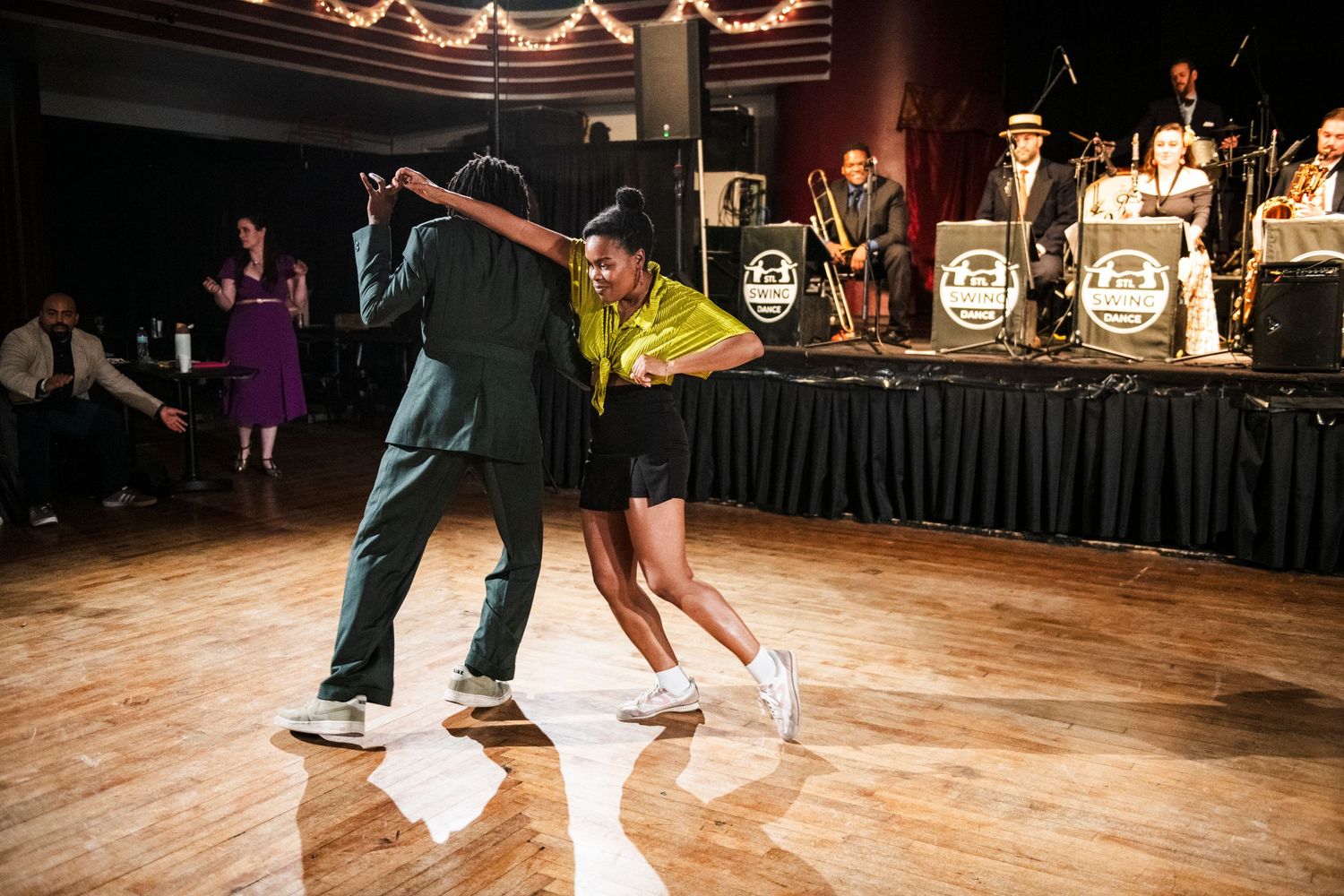 Dancers perform an energetic swing dance routine in front of a live orchestra.
