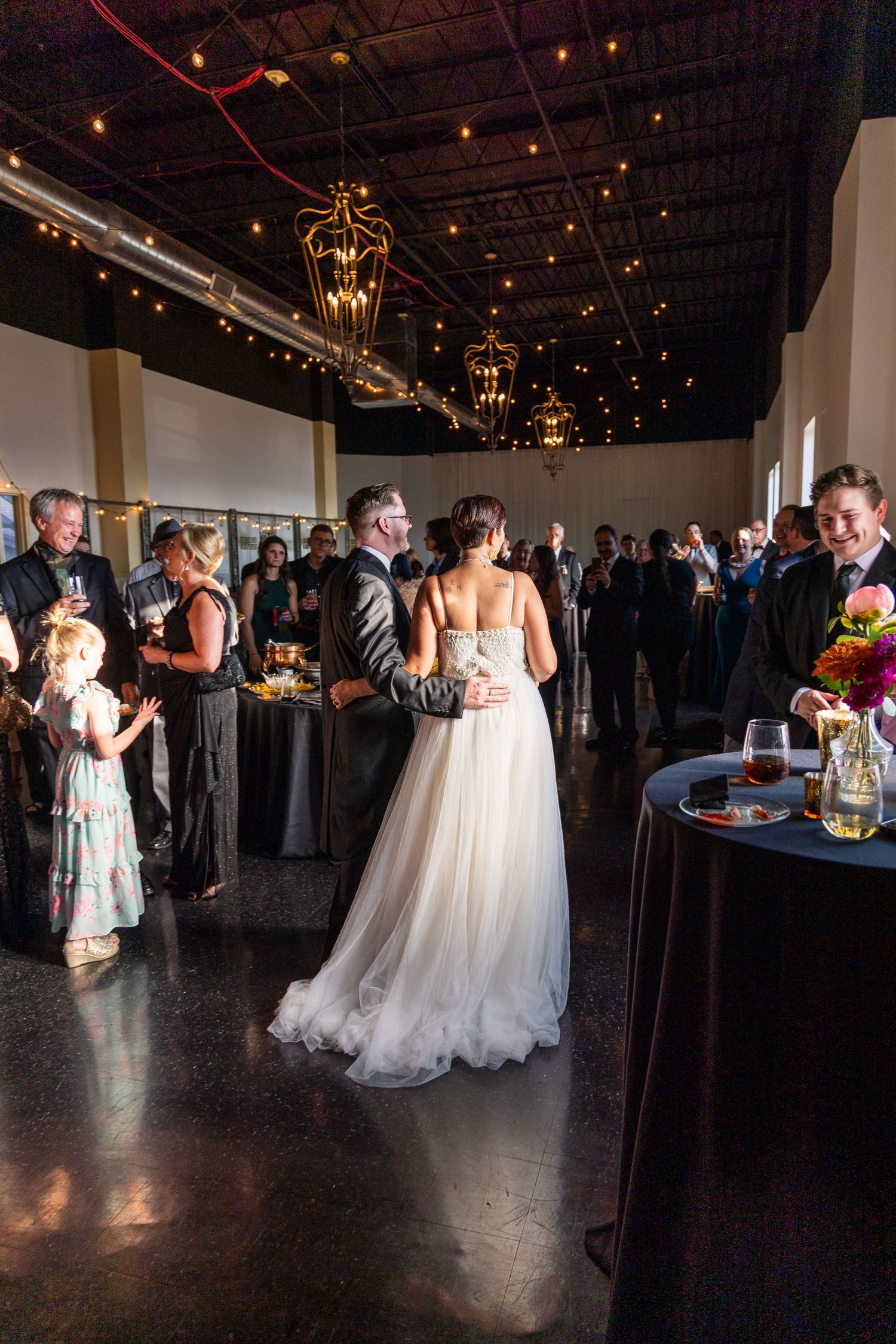 Wedding reception venue with elegant chandeliers and guests mingling around tables.