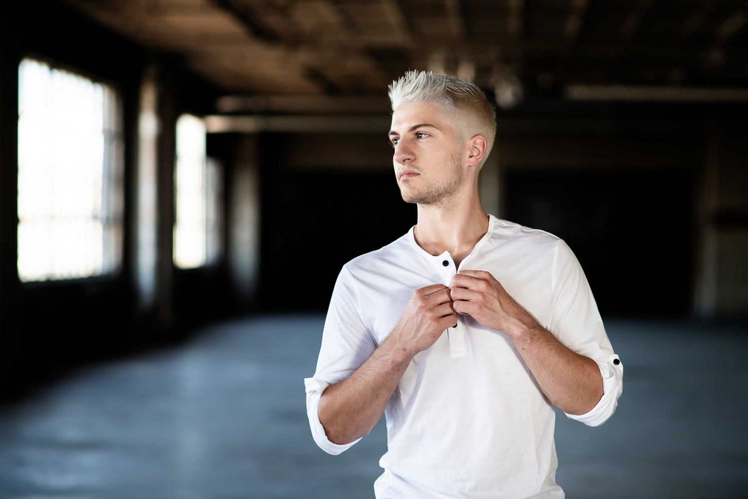 Person in white shirt adjusting collar while standing in an empty industrial space with natural lighting.