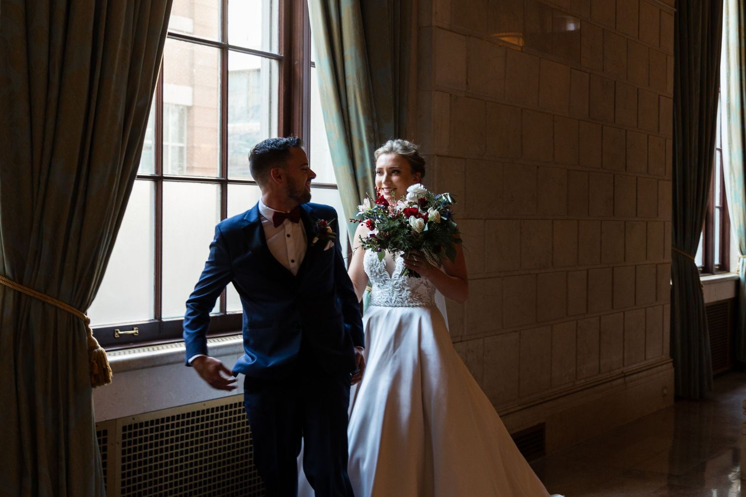Romantic moment between newlyweds in an ornate hallway with natural window light.