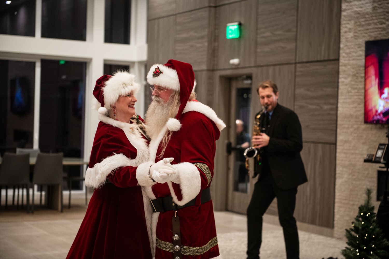 Two people in Santa costumes interacting at holiday celebration indoors.