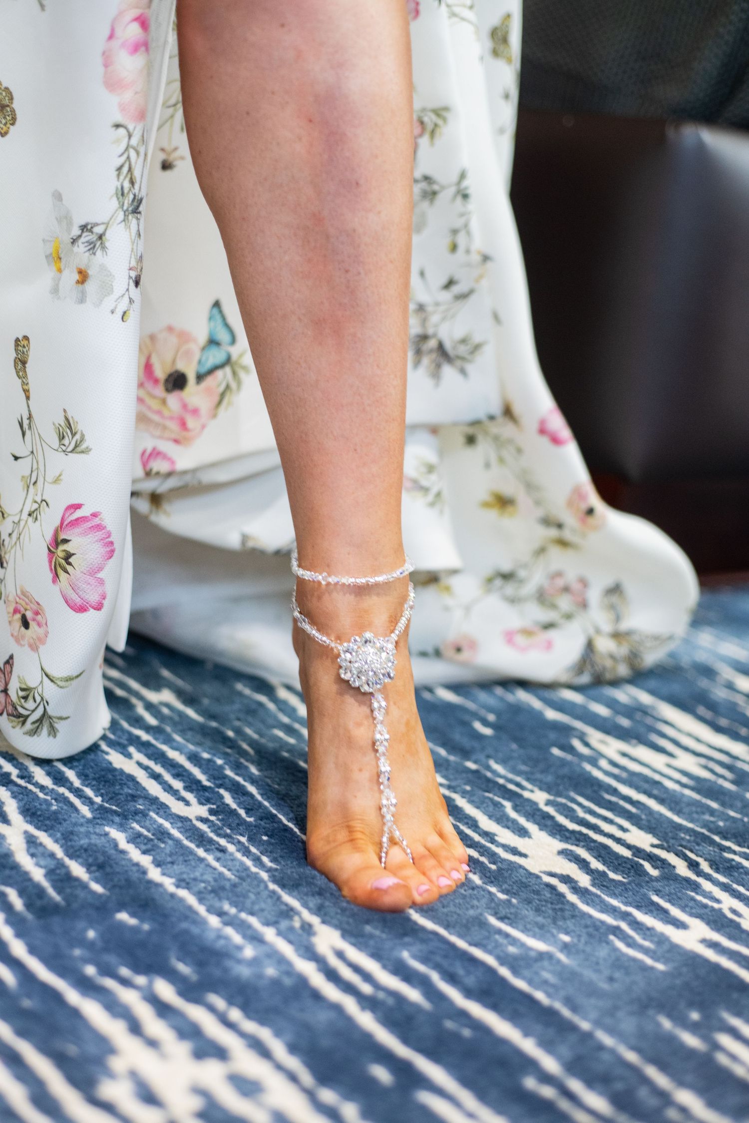 Decorative barefoot anklet jewelry against blue distressed wood flooring.