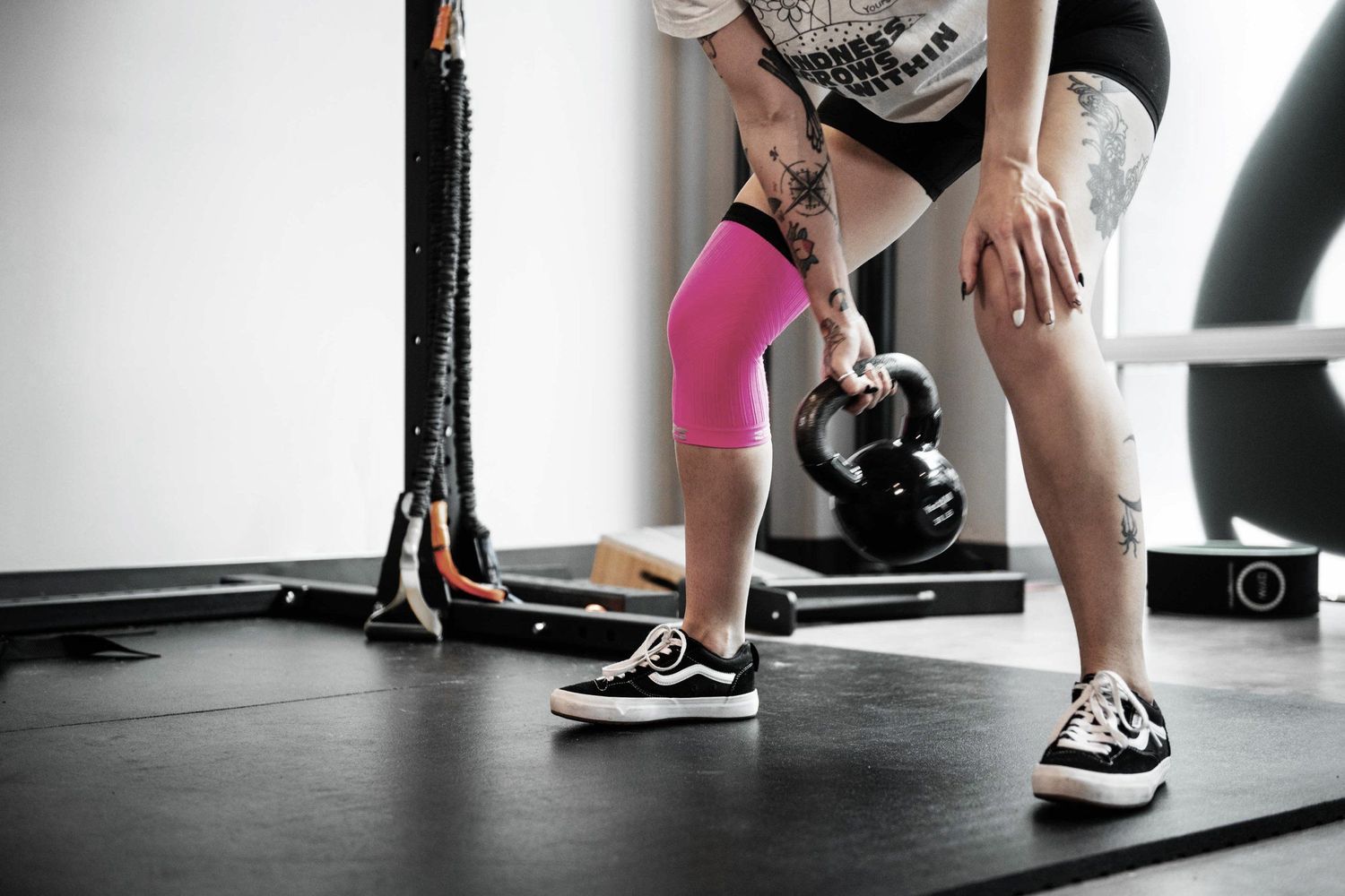 Person wearing pink kinesiology tape performing kettlebell exercise in gym.