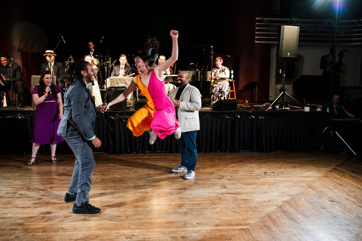 Swing dancers in colorful dresses perform dynamic lifts and spins on a dance floor.