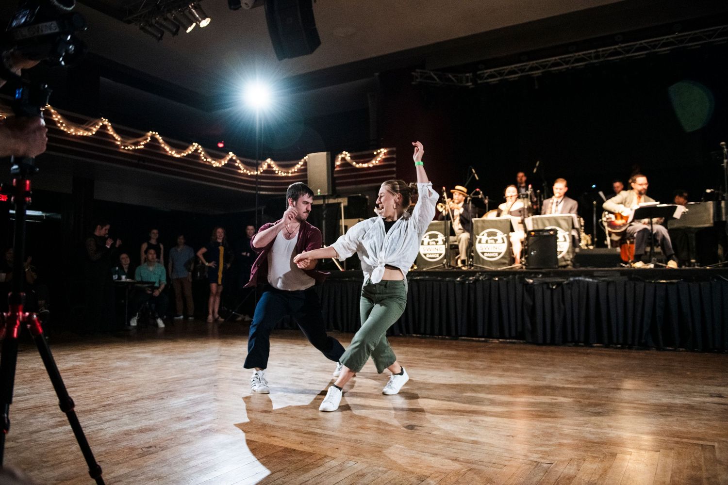 Swing dance partners execute an energetic dance move under stage lighting.