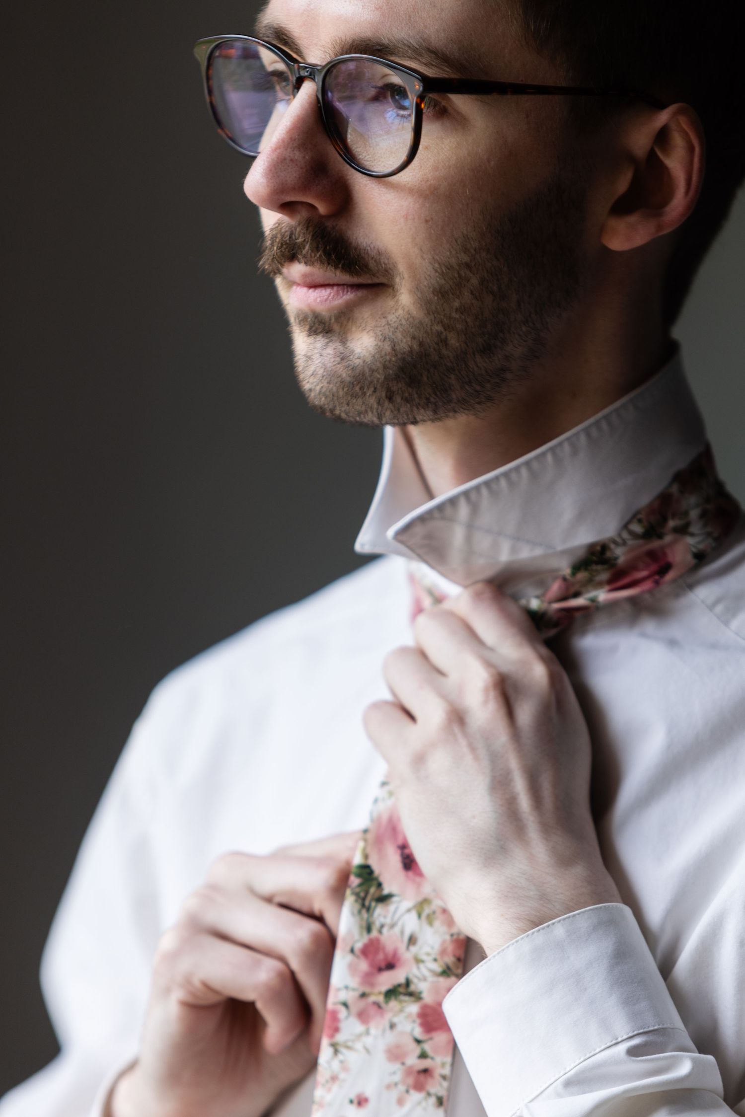 Portrait showing detail of floral tie and white collar shirt against dark background.