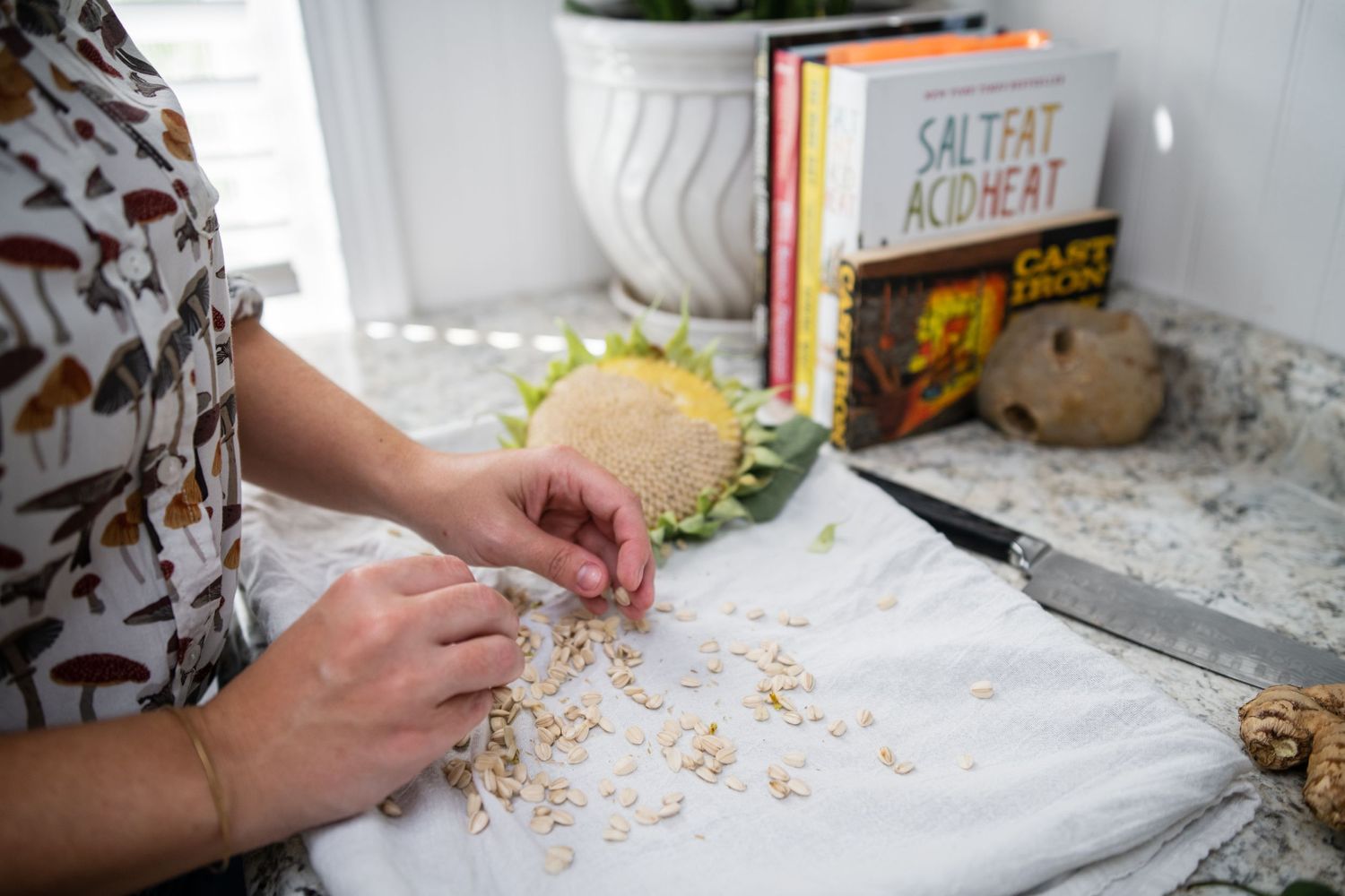 Hands preparing food ingredients on a white cutting board with cookbooks nearby.