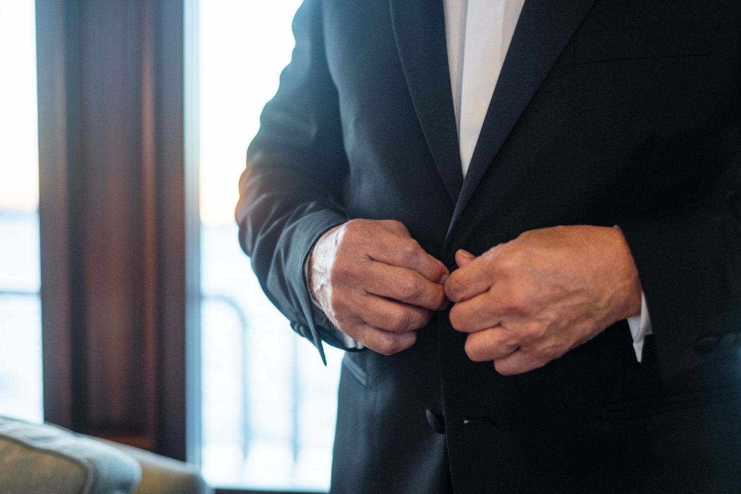 Person in dark suit jacket adjusting buttons near window.