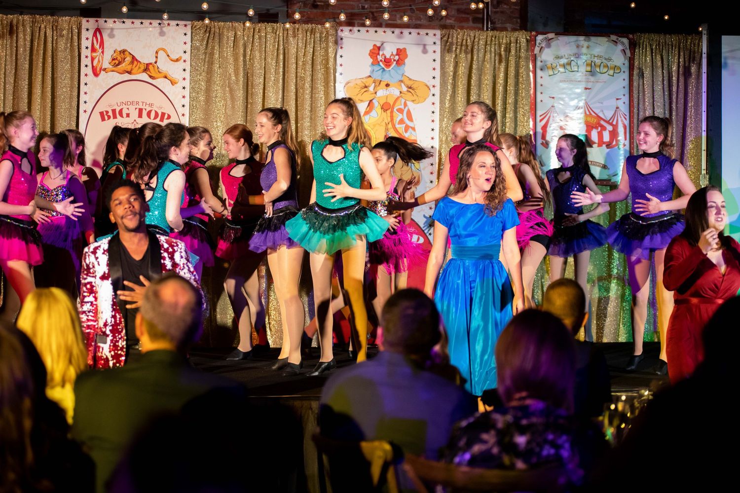 Colorful performance on stage with dancers in vibrant dresses under theatrical lighting.