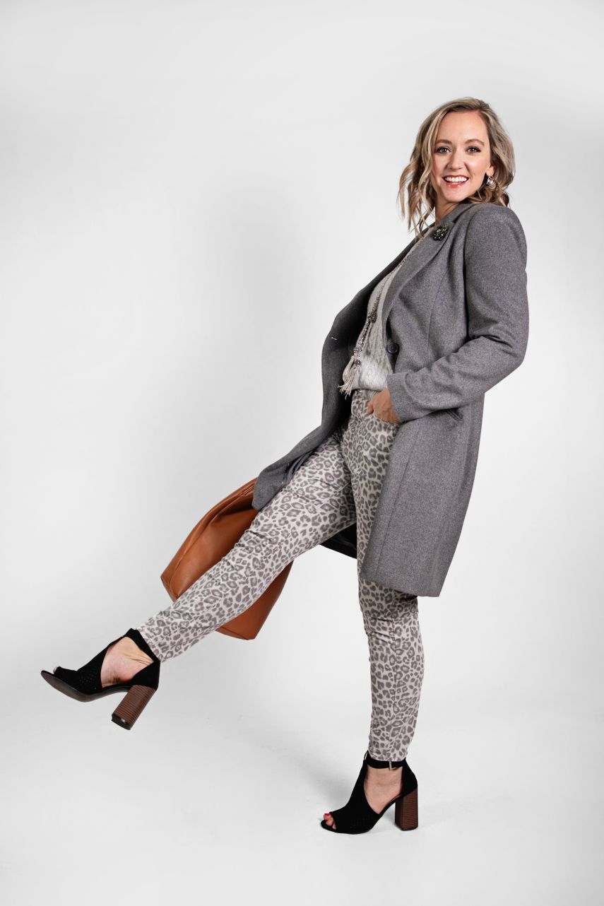 Stylish outfit featuring grey coat, leopard print pants and black heels in fashionable pose against white background.