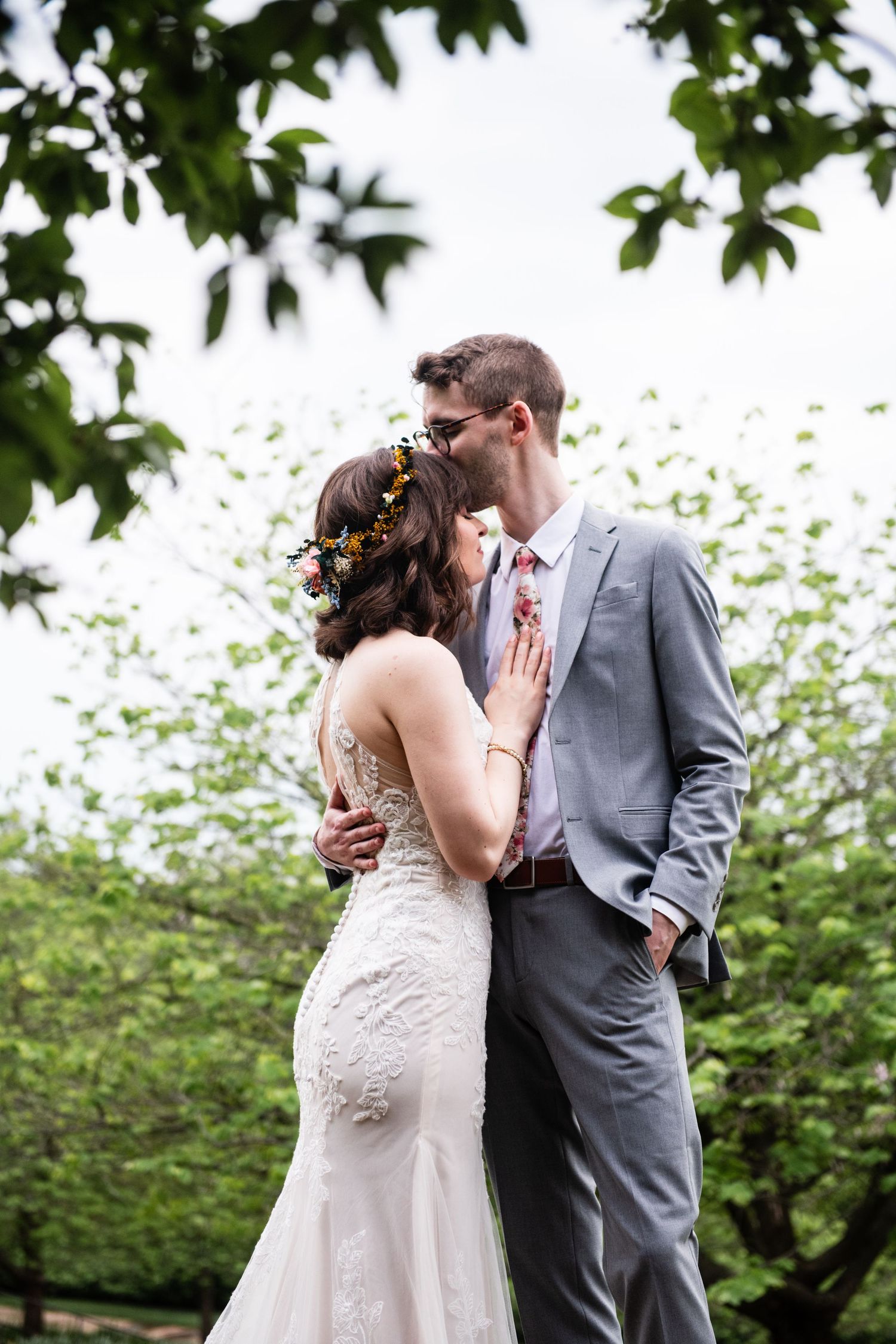 Romantic wedding portrait under tree canopy with bride wearing lace dress.