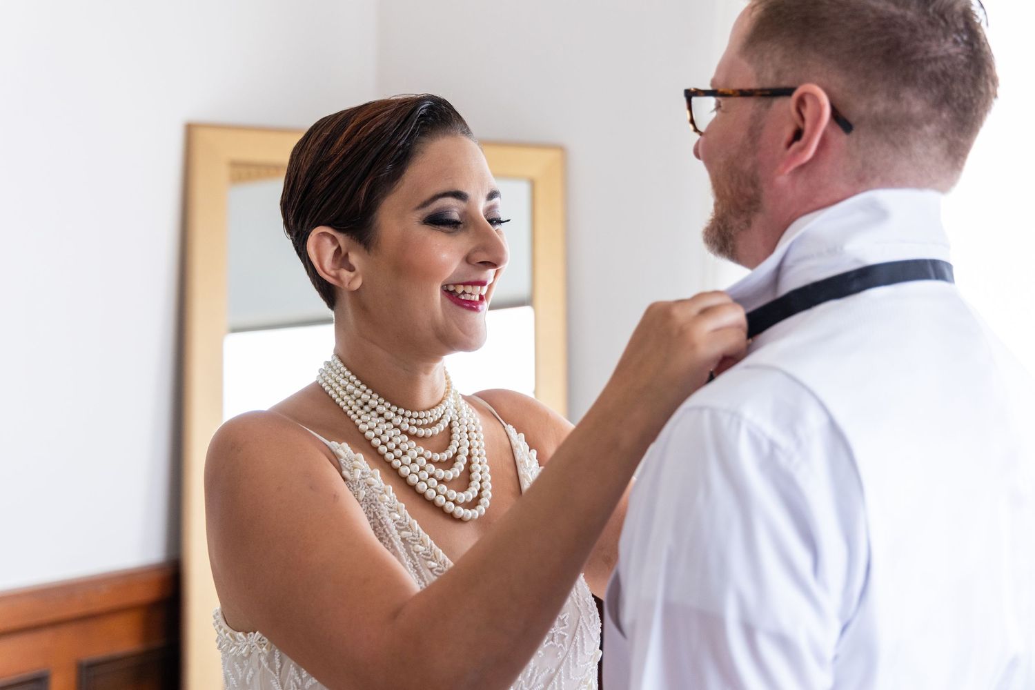 Wedding preparation moment with bow tie adjustment in natural light.