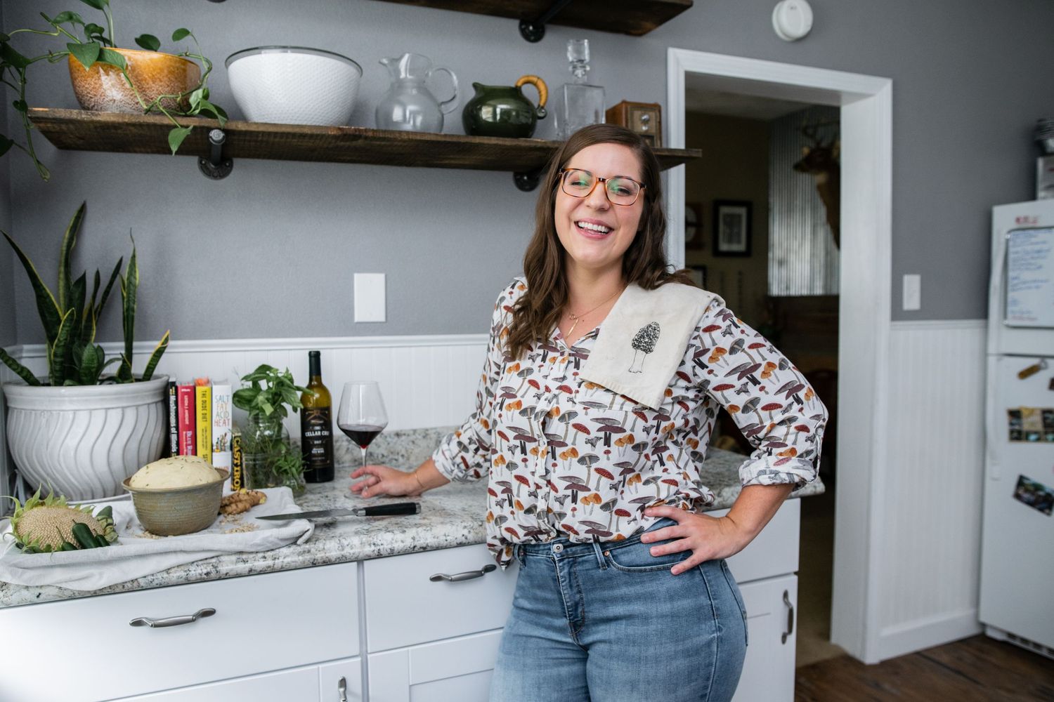A floral-patterned top and denim jeans in a modern white kitchen with floating wood shelves and gray walls.