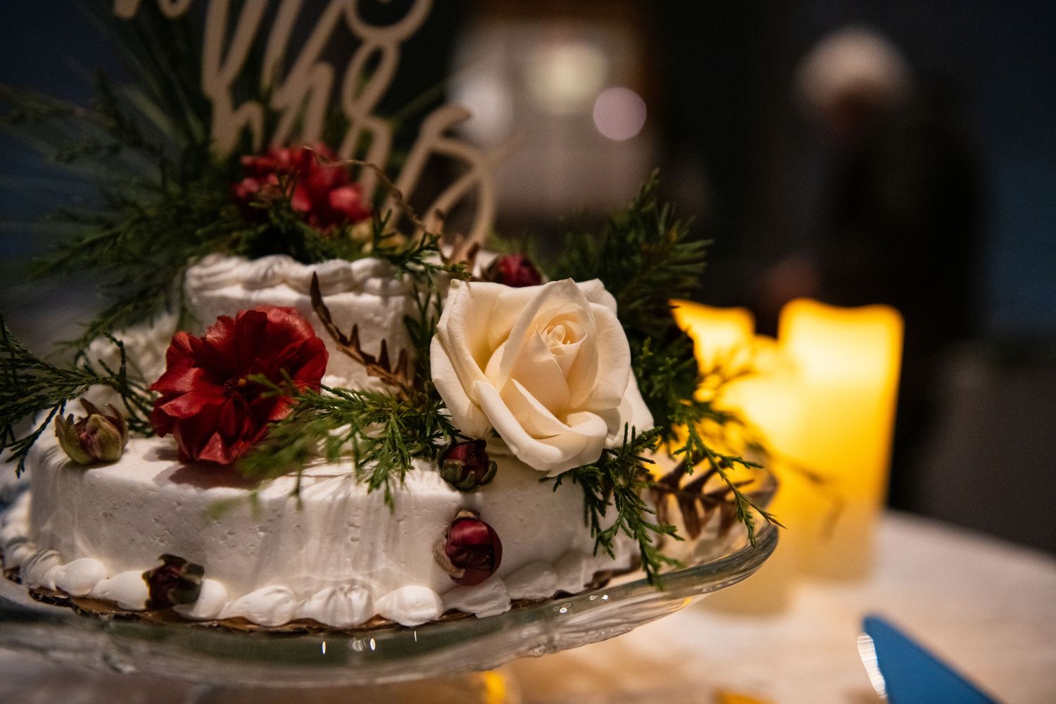 Close up of wedding table centerpiece with peach rose and red berries next to glowing candle.