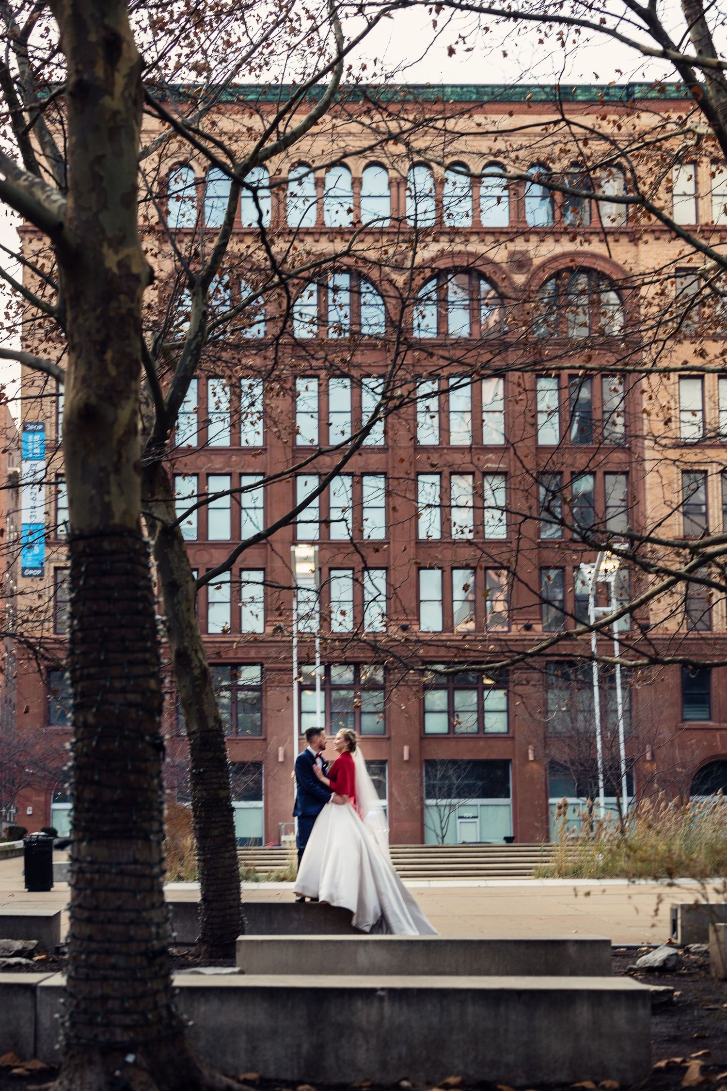 Elegant winter wedding portrait with historic brick building backdrop.