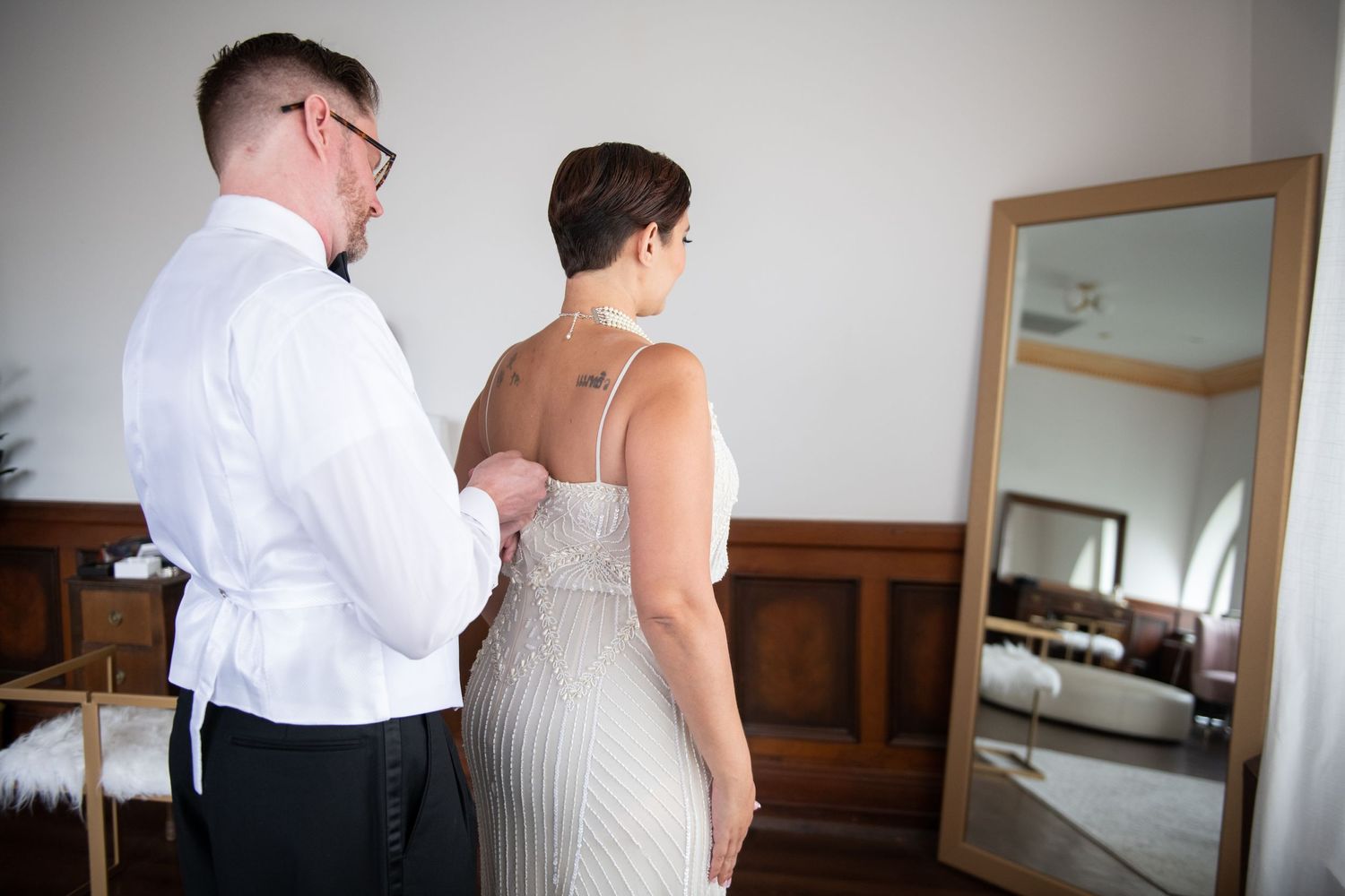 A close-up of a white beaded wedding dress being buttoned up before the ceremony.
