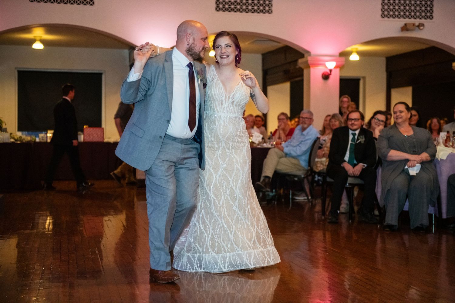 A couple dances energetically on a polished ballroom floor during their wedding reception.