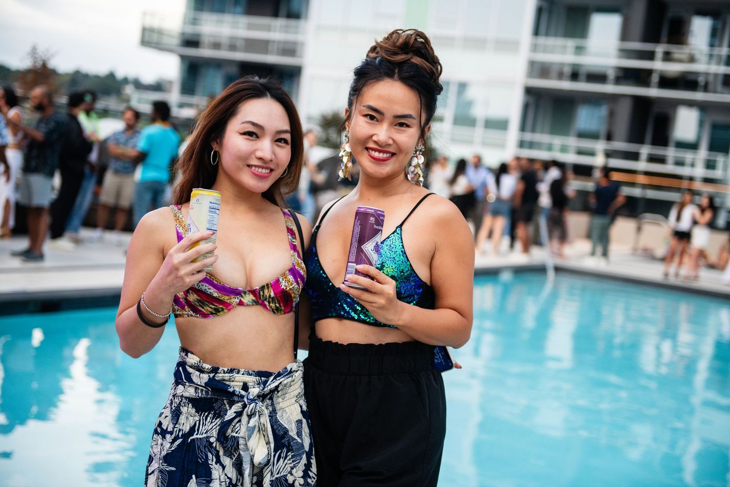 Friends enjoying drinks by a rooftop pool with city buildings in the background.